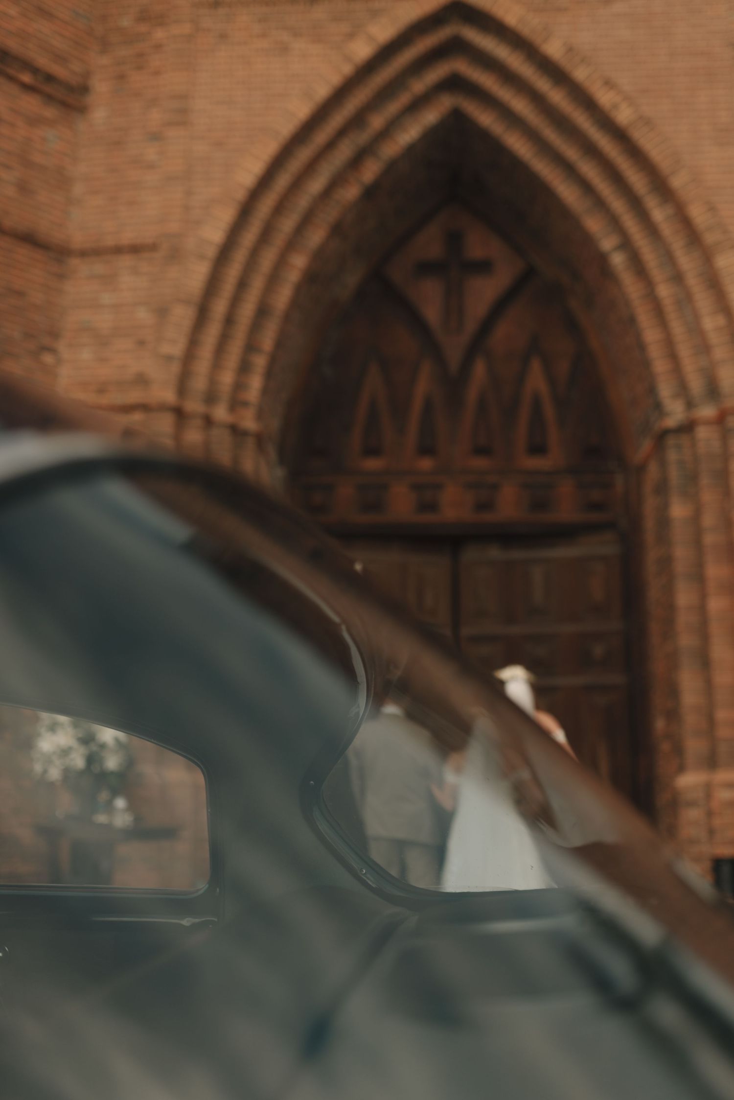 Architectural detail of a Gothic church entrance with pointed arches and brick construction visible through car reflections.