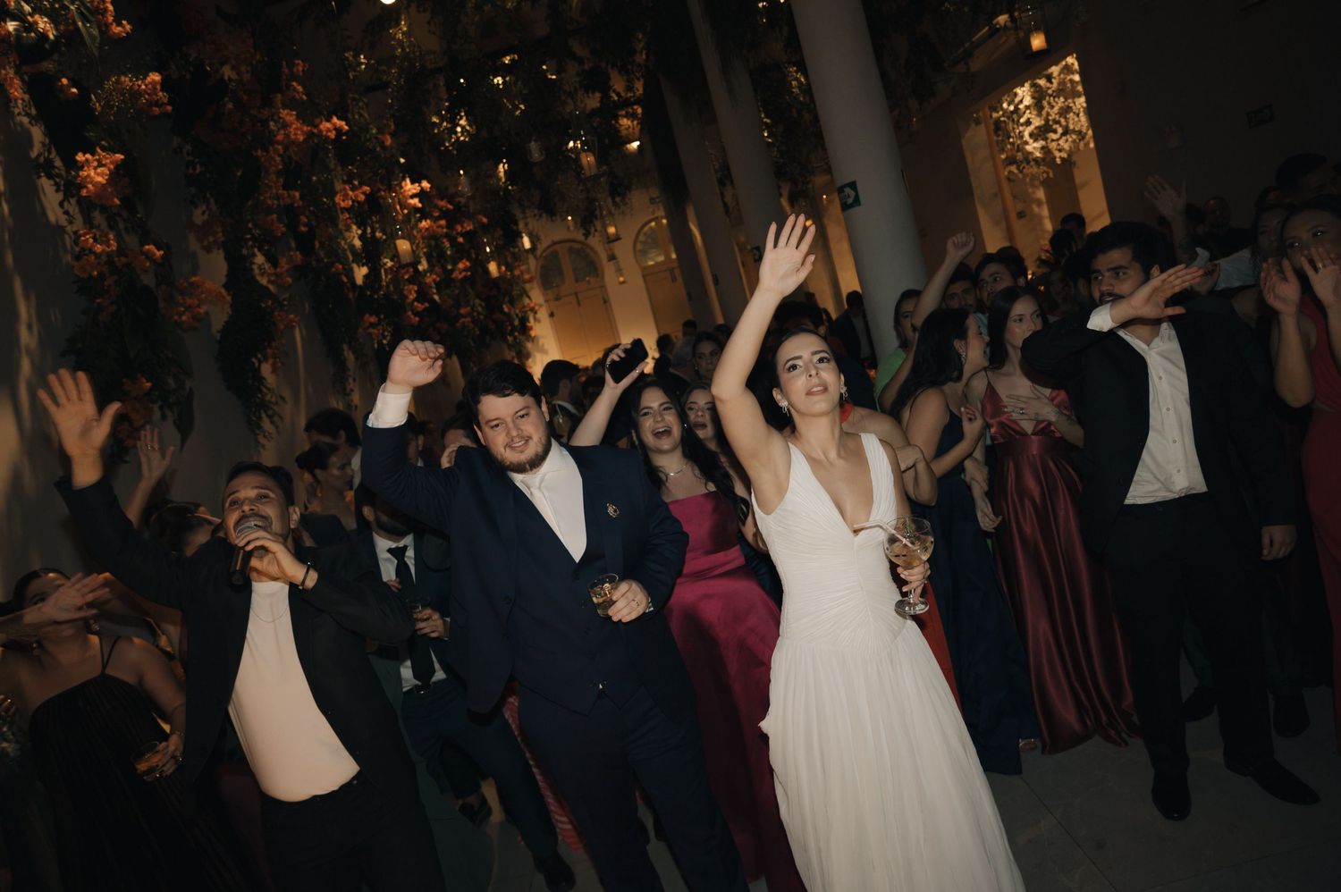 Wedding guests dance and celebrate on a dimly lit dance floor during an evening reception celebration.