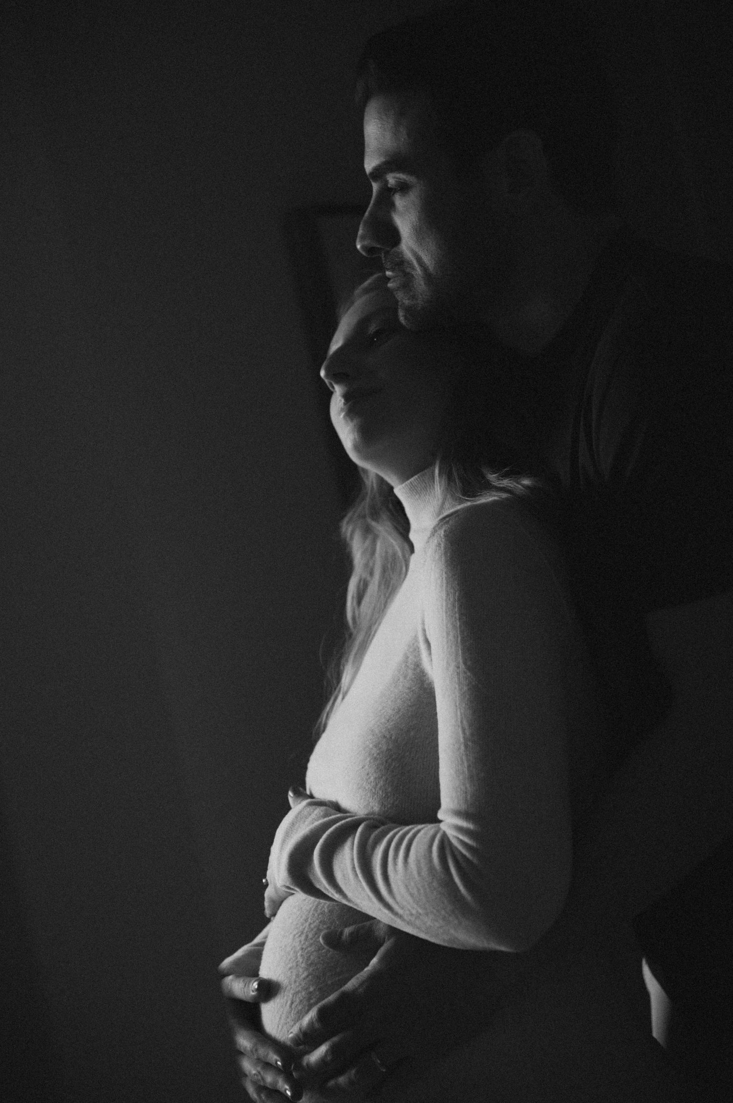 Intimate black and white maternity portrait captures tender moment between couple.