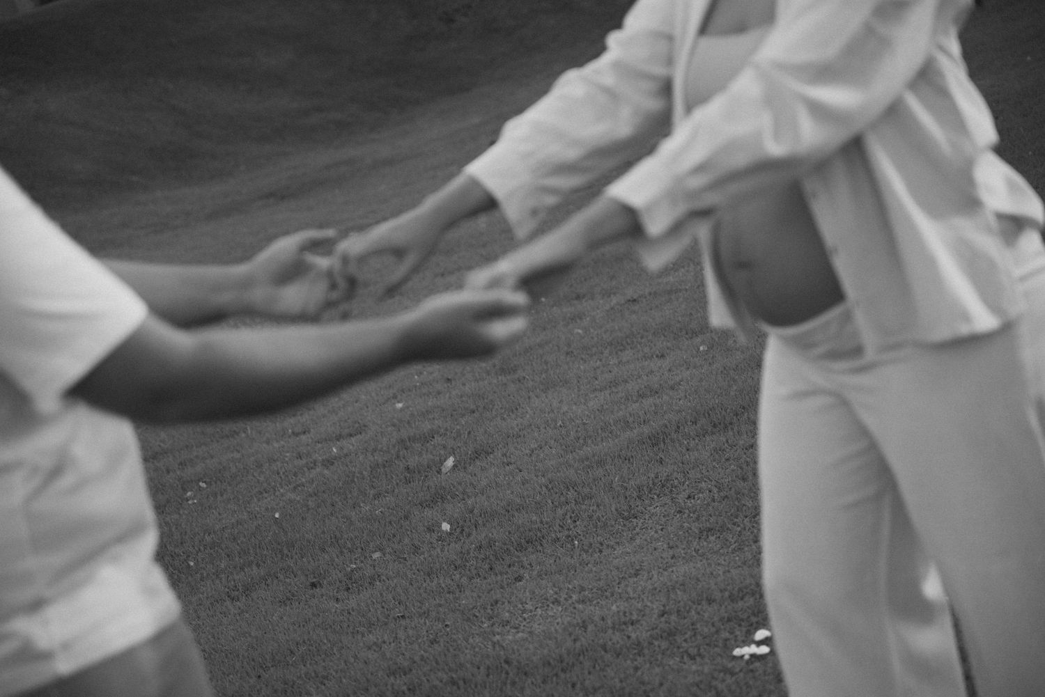 Close-up of hands tenderly touching in white clothing against dark background.