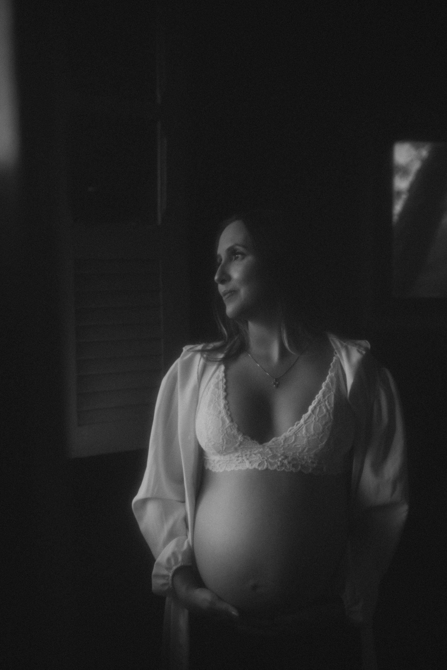 Artistic black and white maternity photo showing expecting mother in white lace top and flowing sleeves.