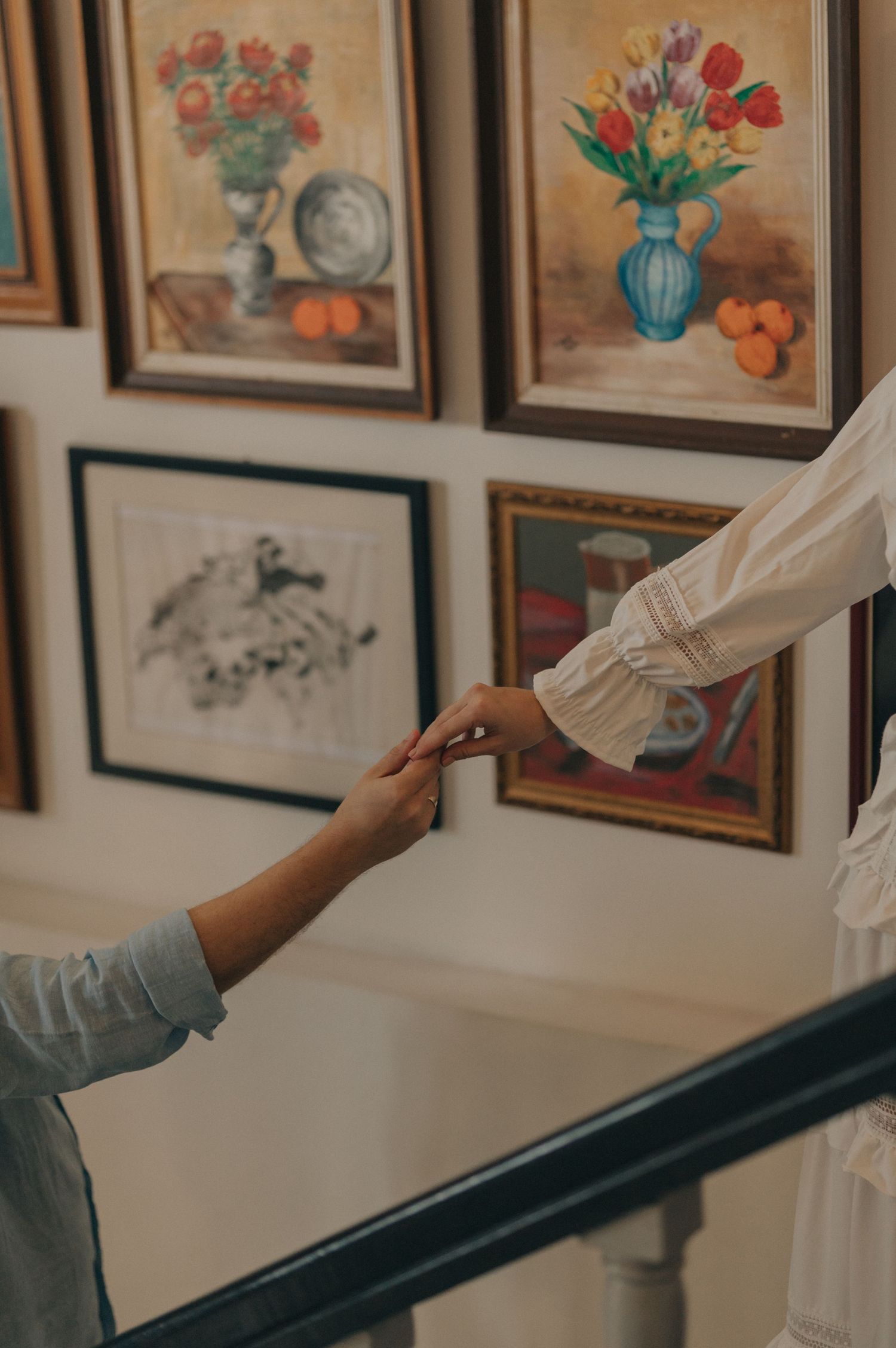 Detail shot of hands reaching towards each other against wall of floral artwork.
