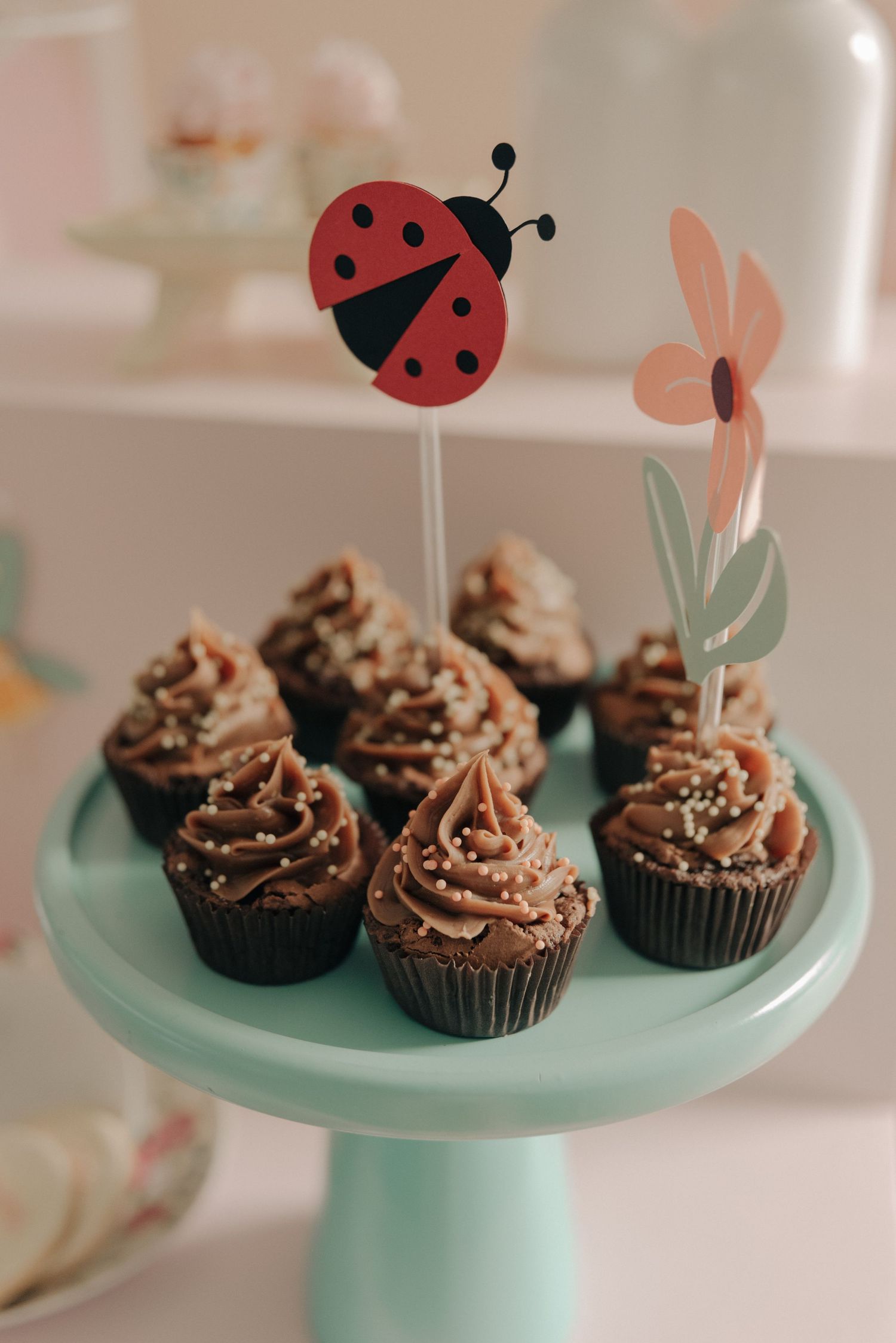 Chocolate cupcakes decorated with frosting on a mint green cake stand with a ladybug cake topper.