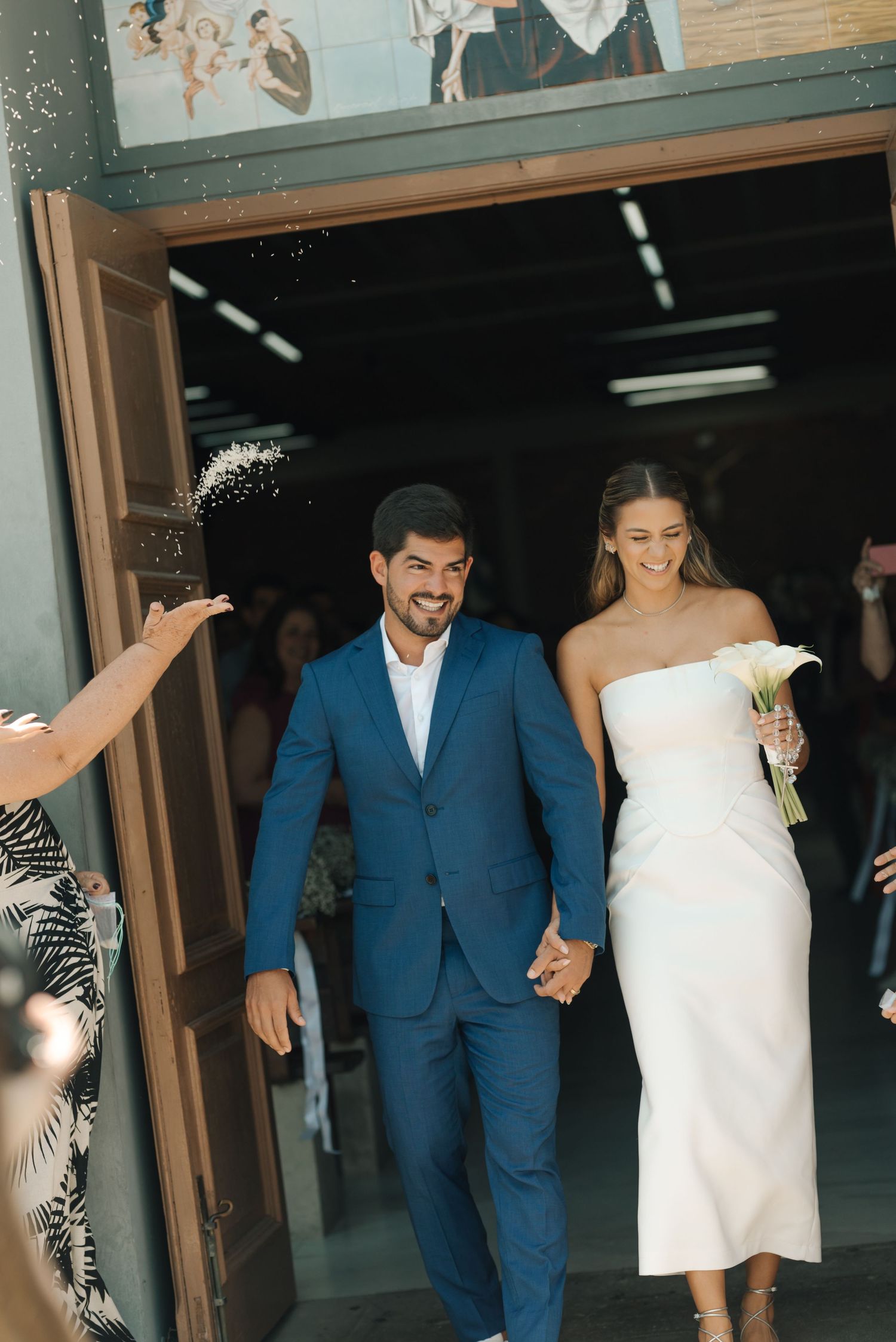 Wedding couple exits venue in stylish attire while guests throw confetti in celebration.