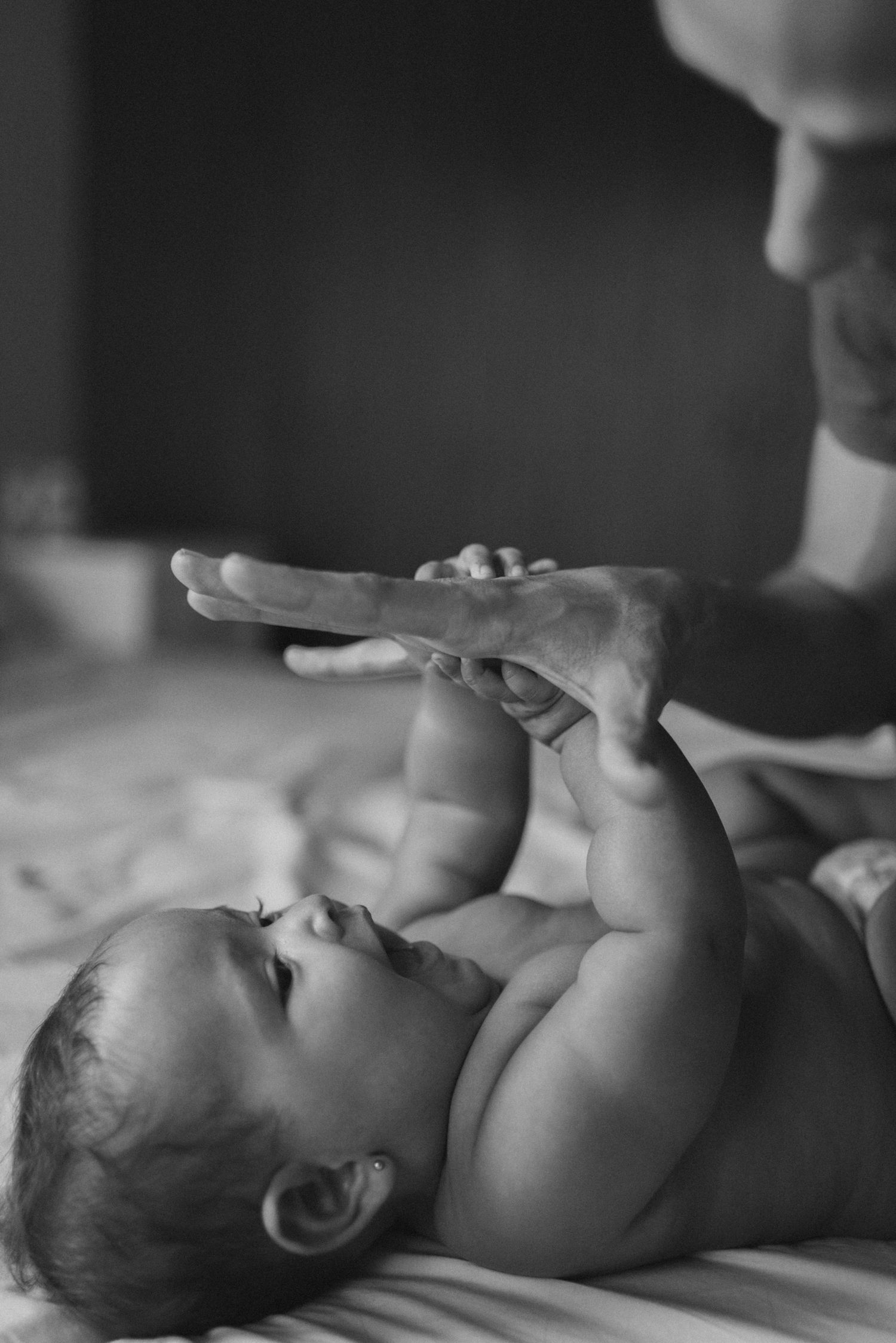 A tender black and white image of a baby reaching up to touch an adult's hand.