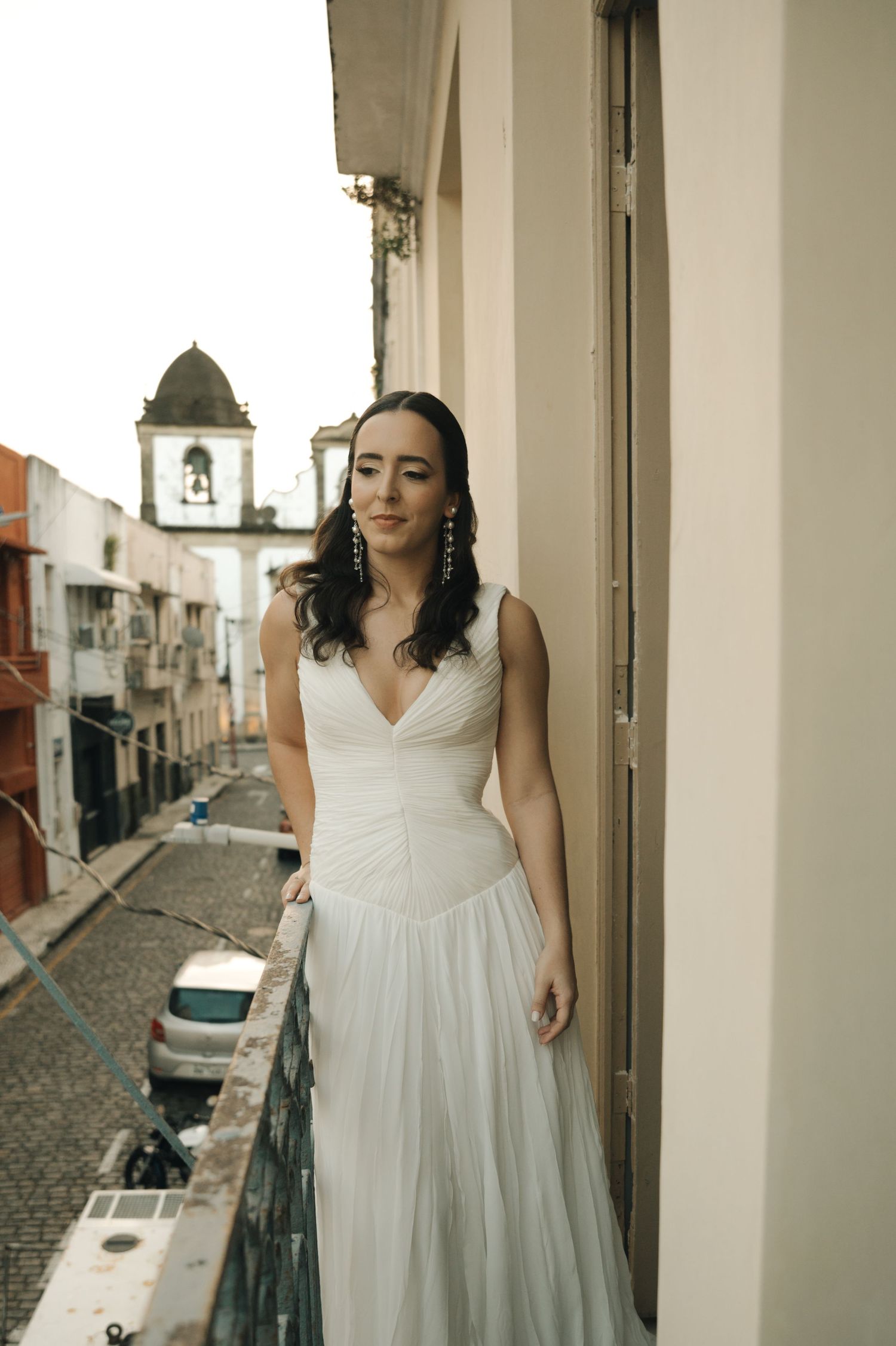 A person in a flowing white wedding dress stands in a doorway overlooking a cobblestone street.