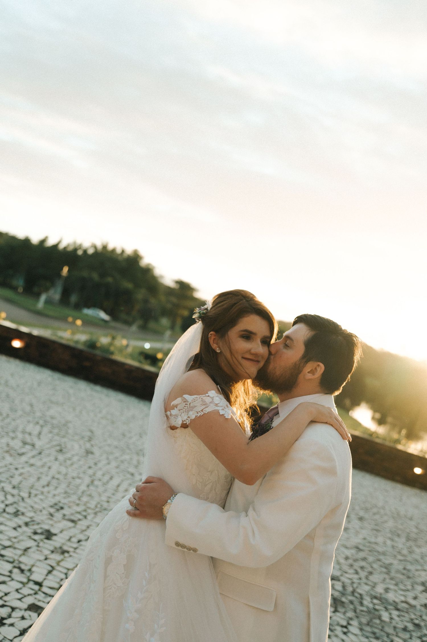 A romantic sunset wedding portrait shows a couple in white embracing against a glowing sky.