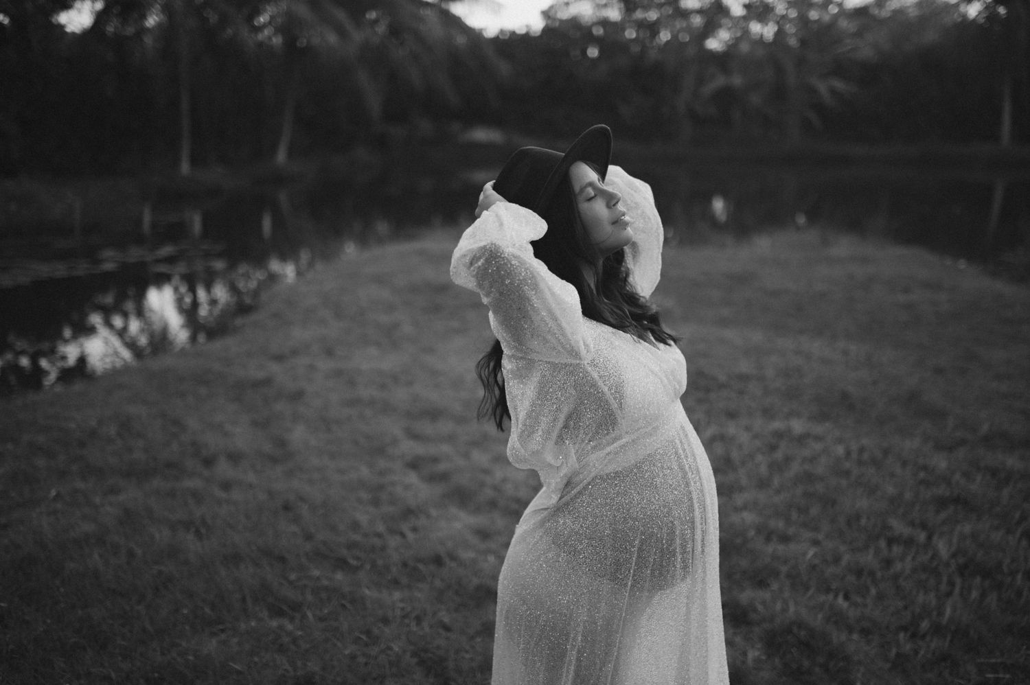 Artistic black and white maternity portrait of woman in flowing dress outdoors.