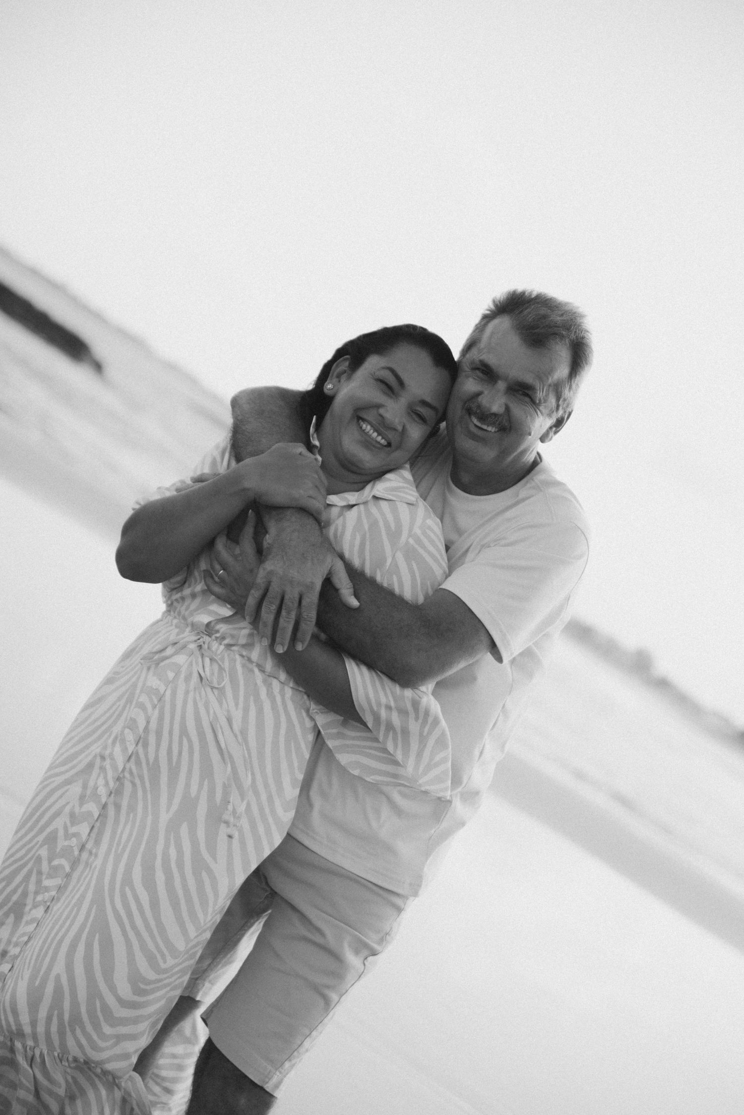 Black and white beach portrait of a happy couple embracing on the shoreline.