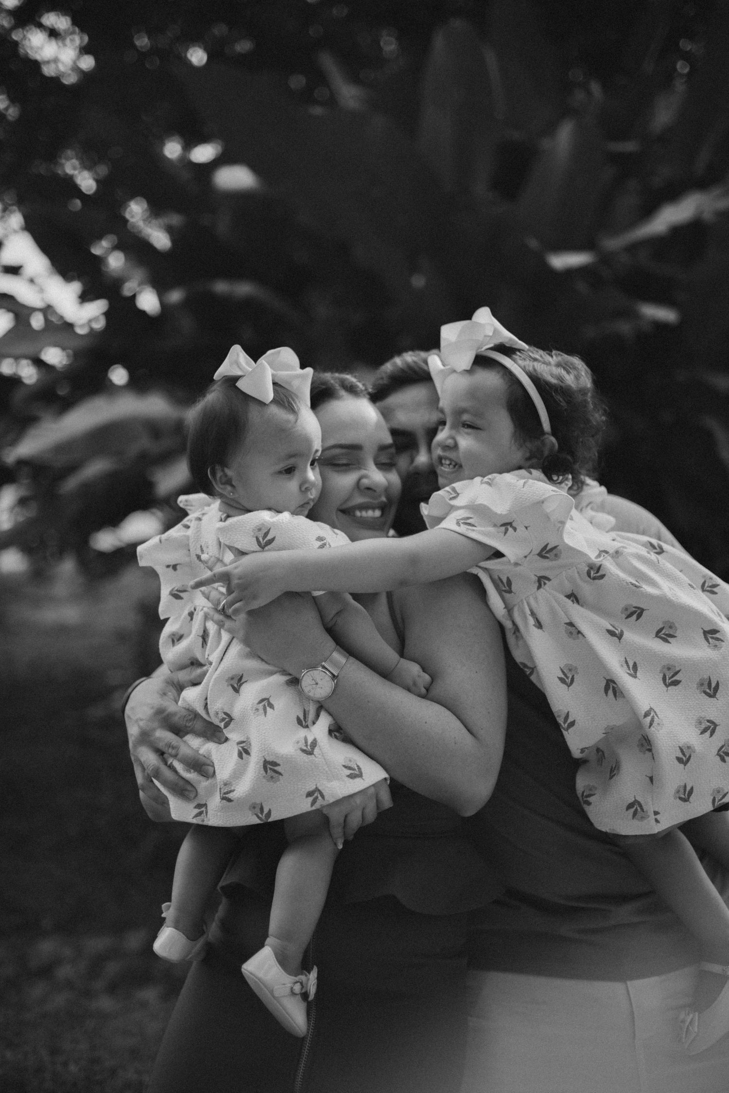 A tender family moment captured in black and white showing matching outfits and loving embraces outdoors.