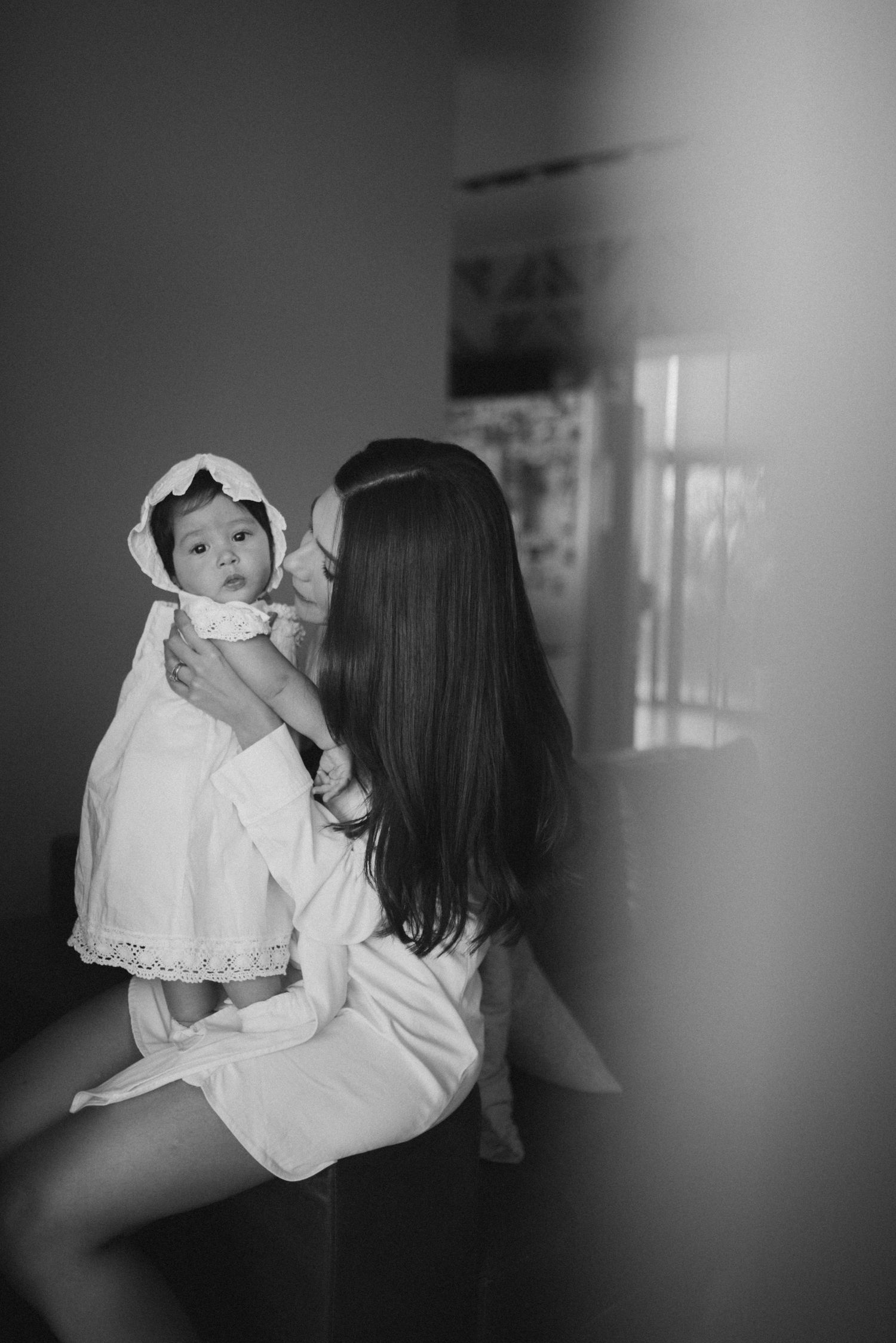 Black and white photo series showing tender moments between parent and baby in white dress against blurred background.