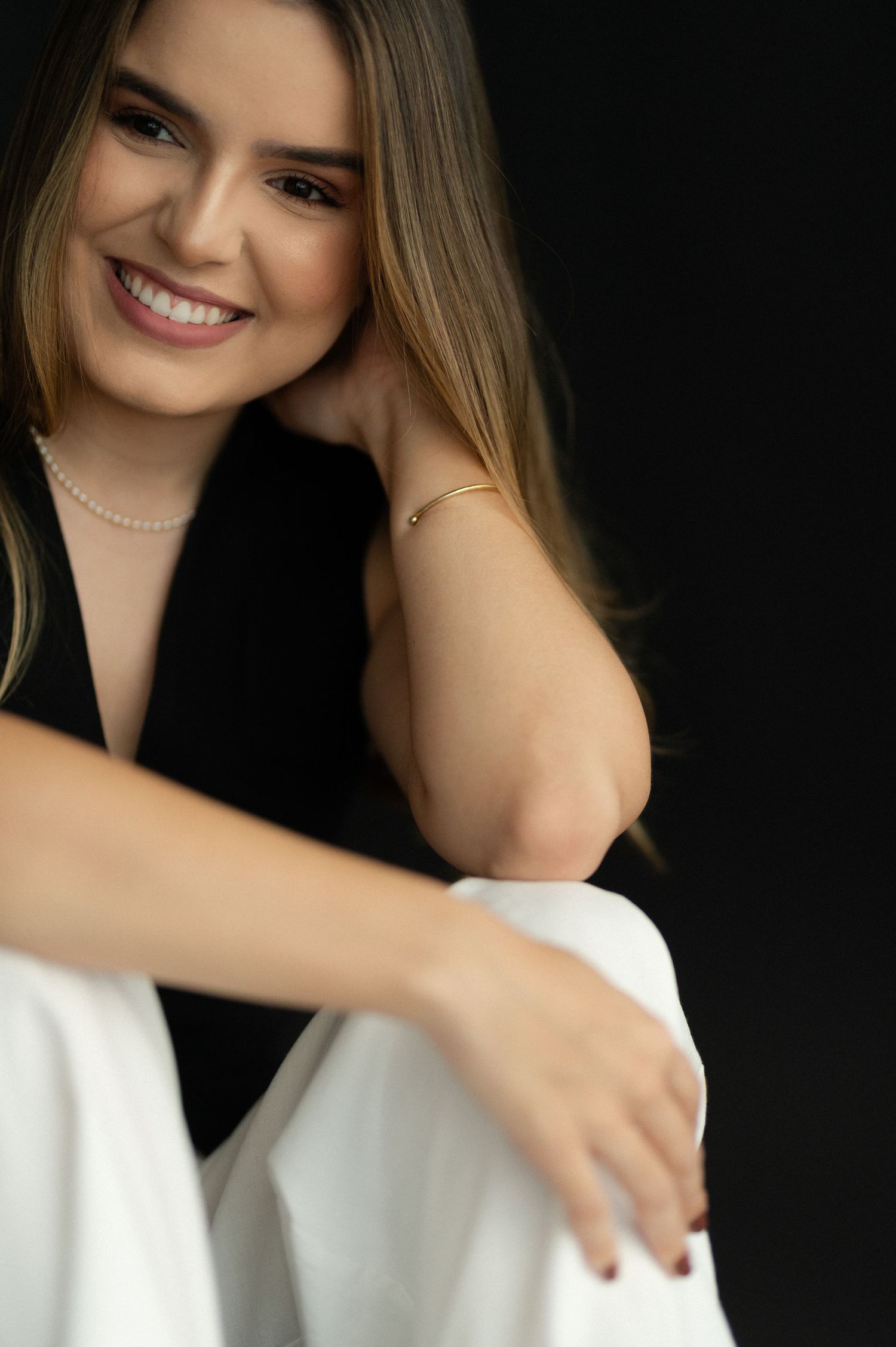Studio portrait featuring a bright smile and pearl necklace against a dark background.