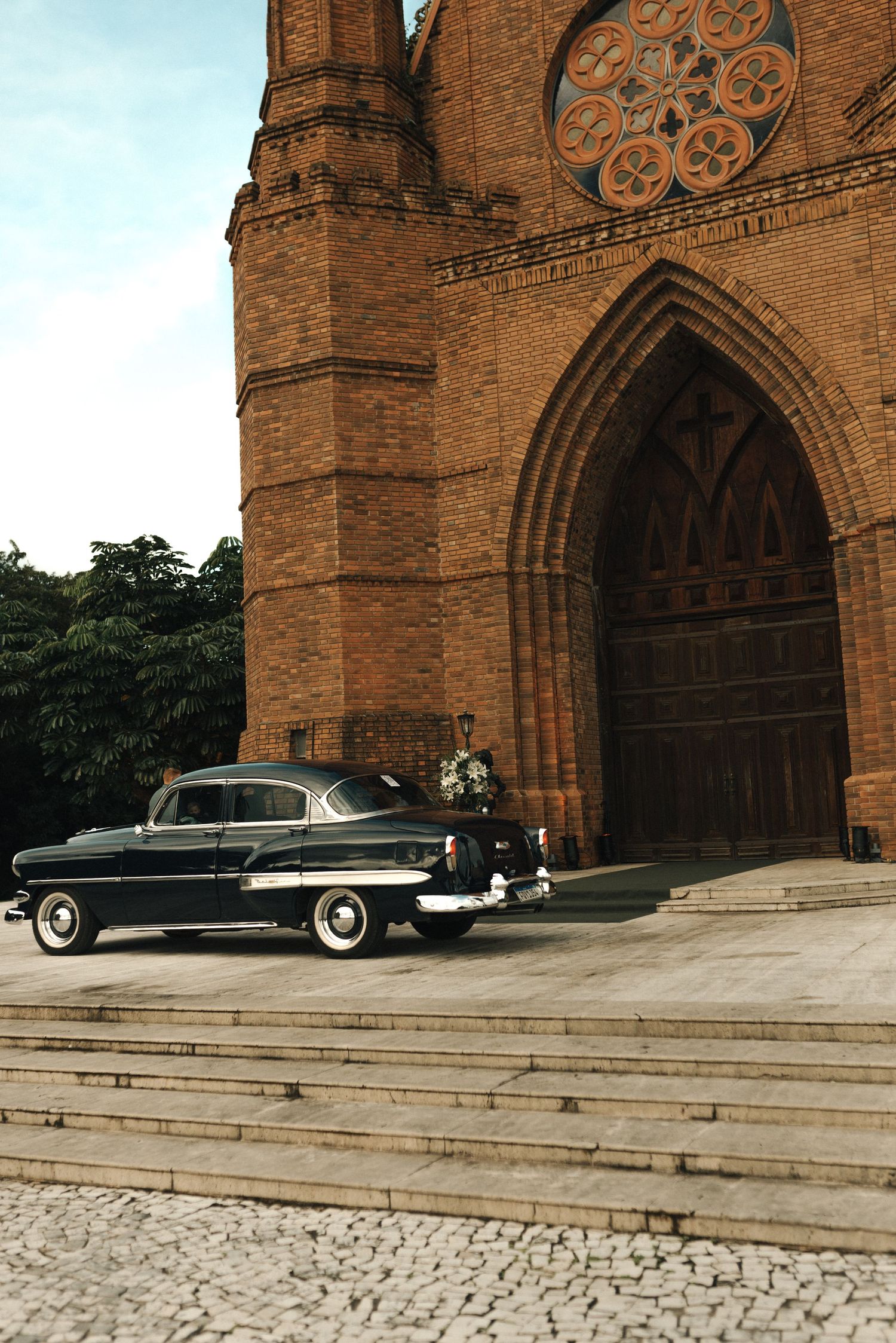 Classic black vintage car parked in front of ornate gothic church archways with stone steps.