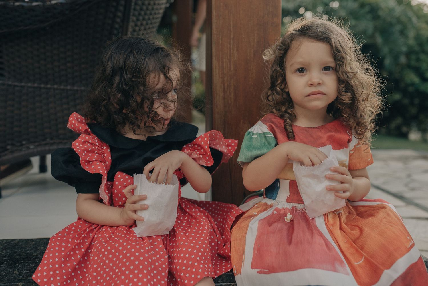 Two children in matching polka dot dresses enjoying drinks outdoors.