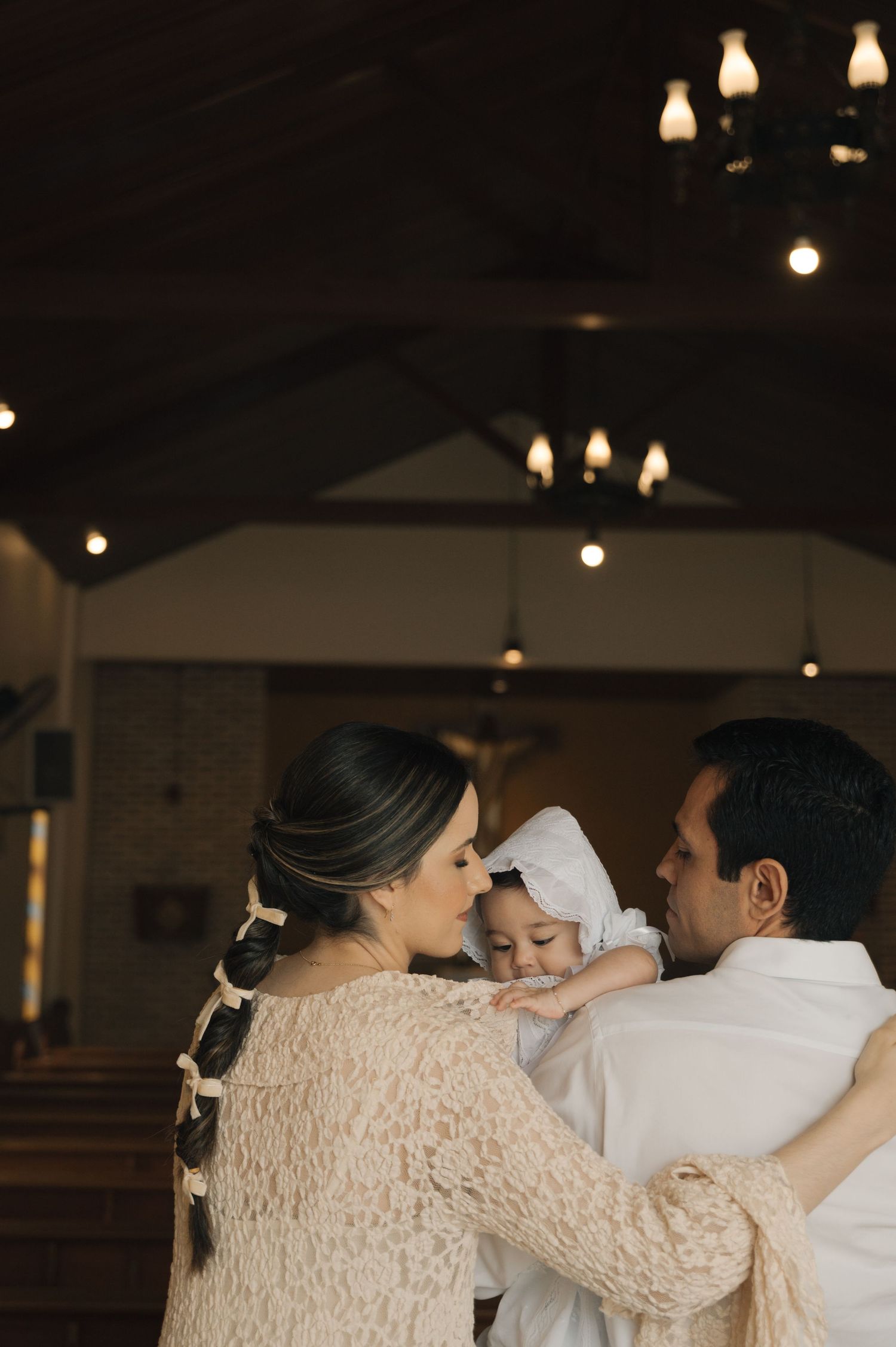 A tender moment in a church interior with soft lighting and glowing pendant lamps overhead.