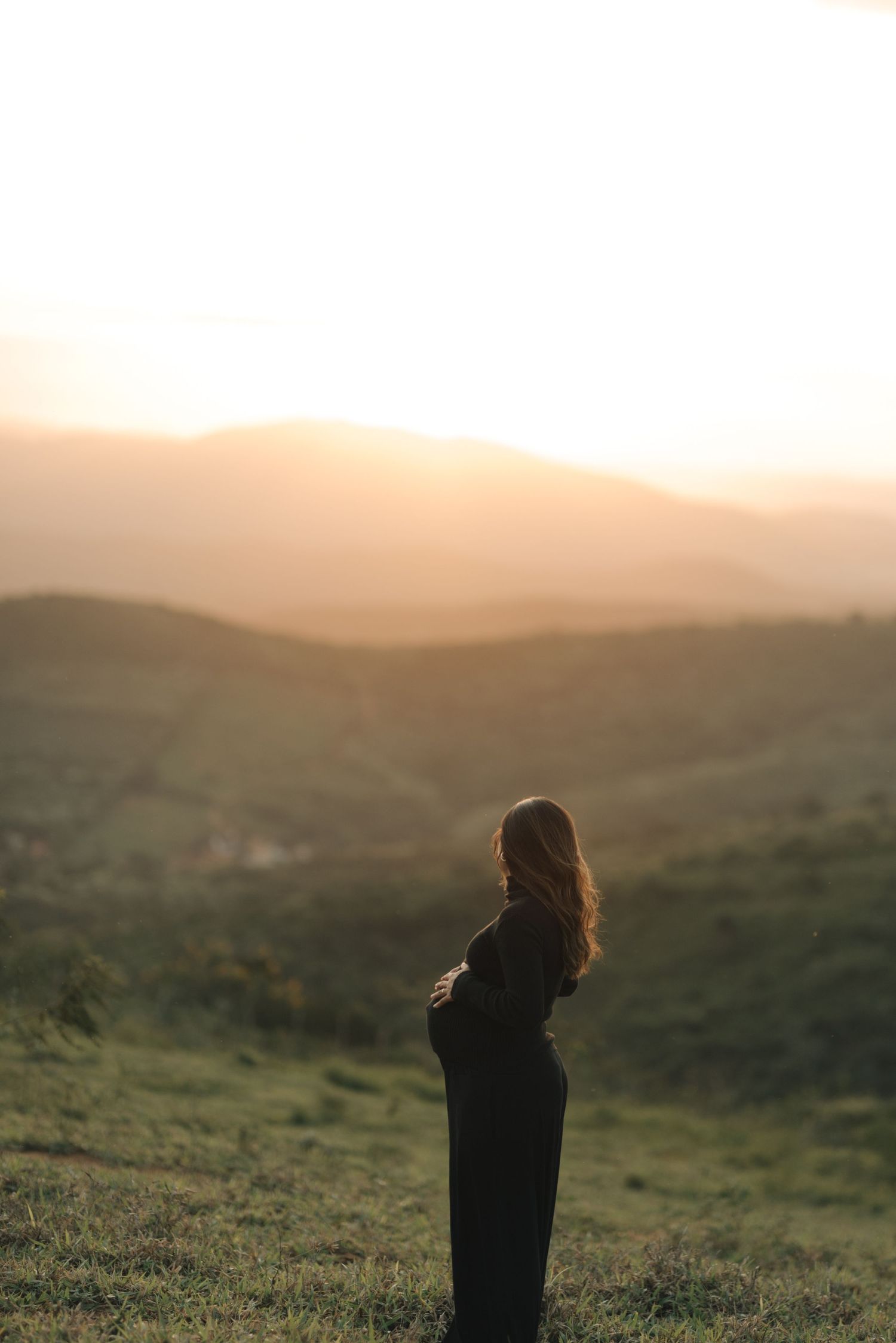 Silhouette of a person standing on a hillside during golden hour.