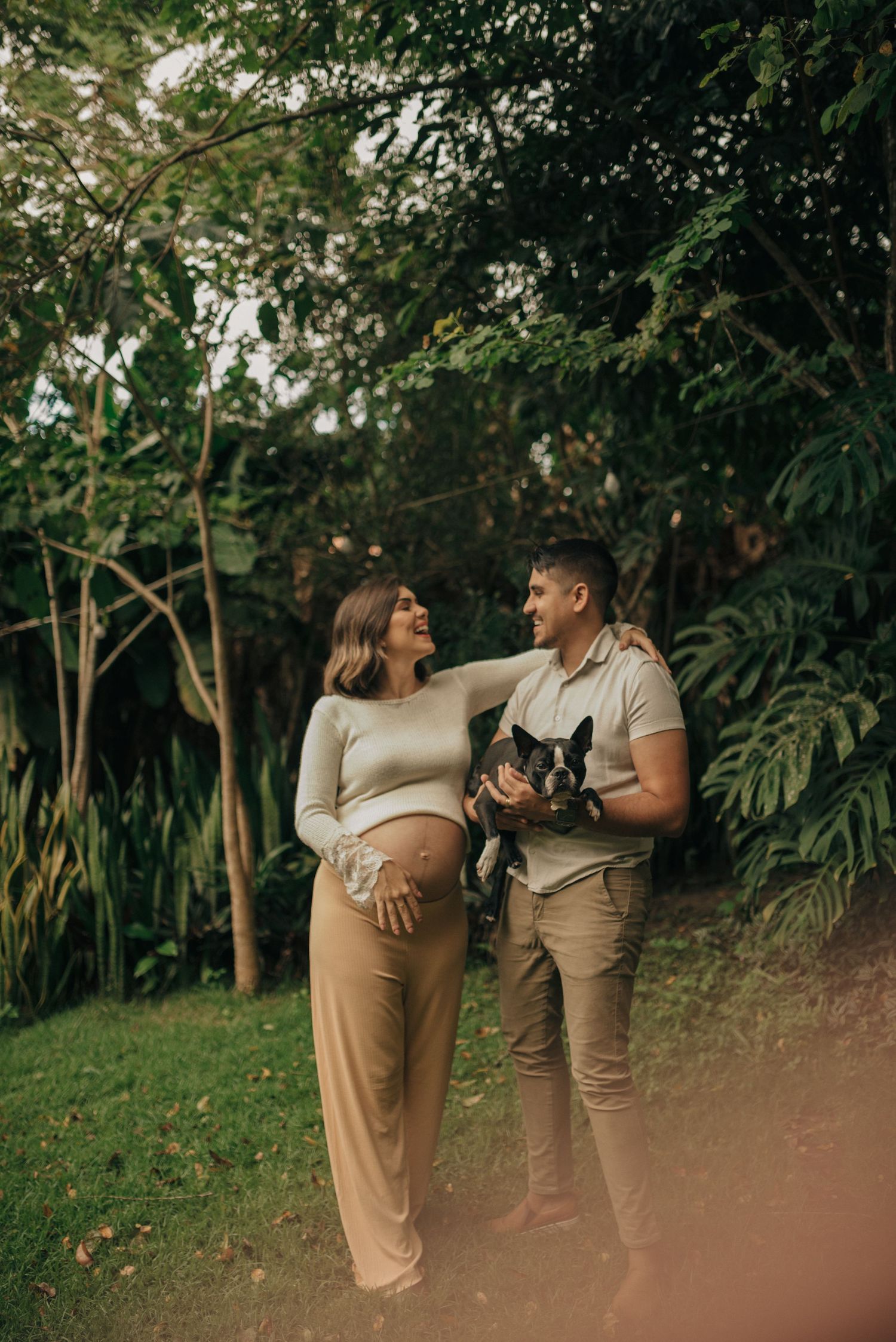 Outdoor maternity photo of couple with pet in lush garden setting.