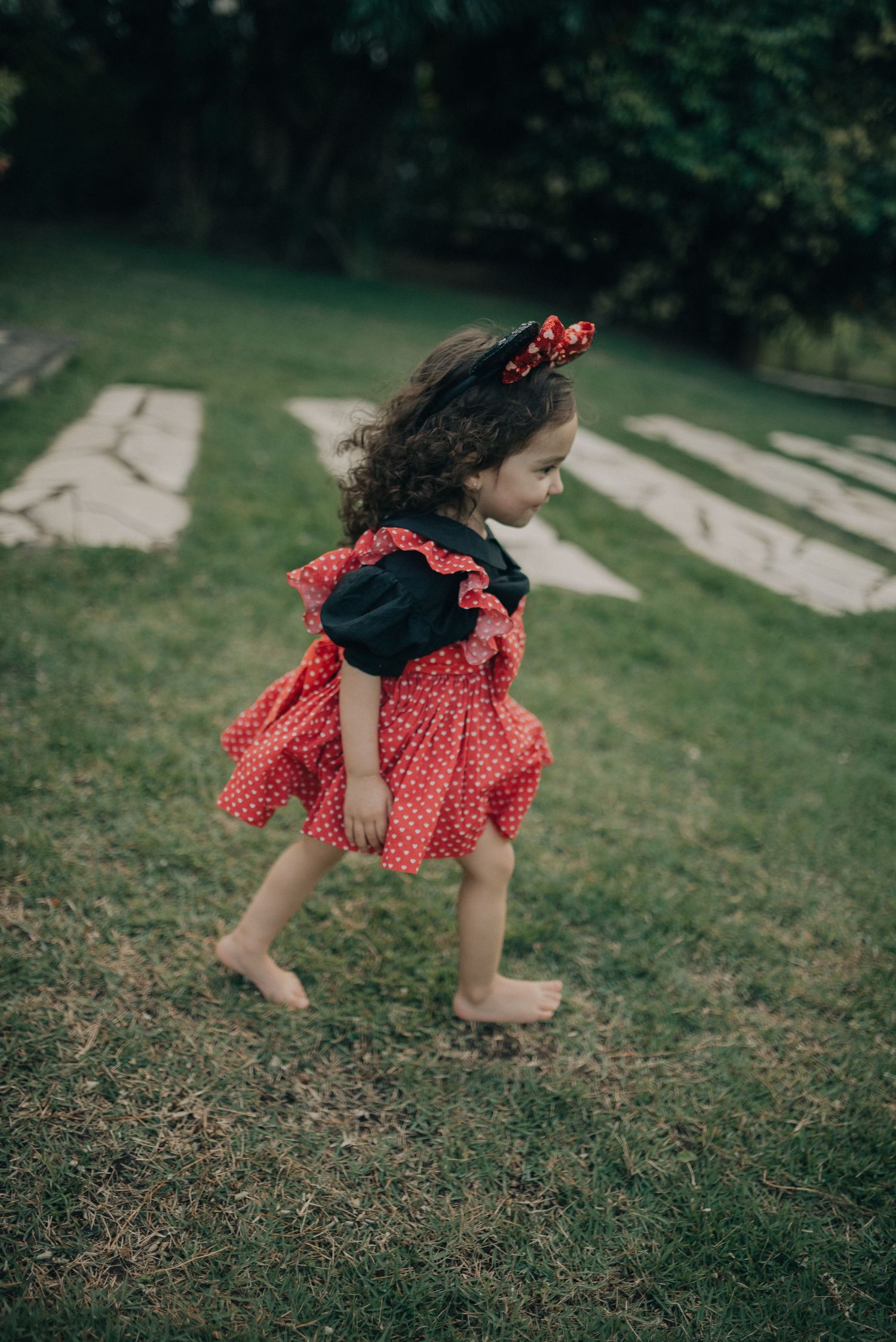 Child in red polka dot dress running barefoot on grass path.
