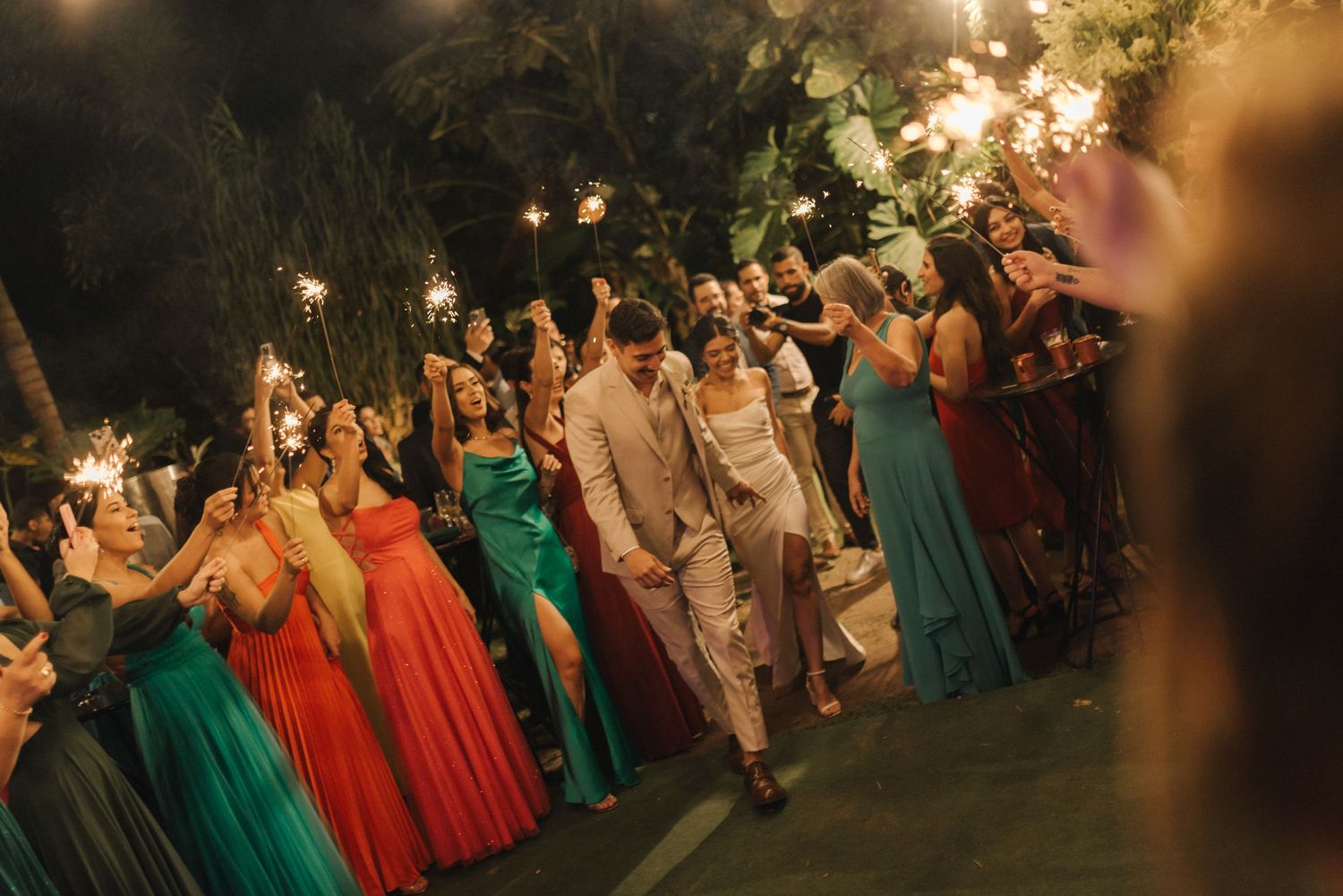 Wedding guests in vibrant dresses celebrate on an illuminated outdoor dance floor.