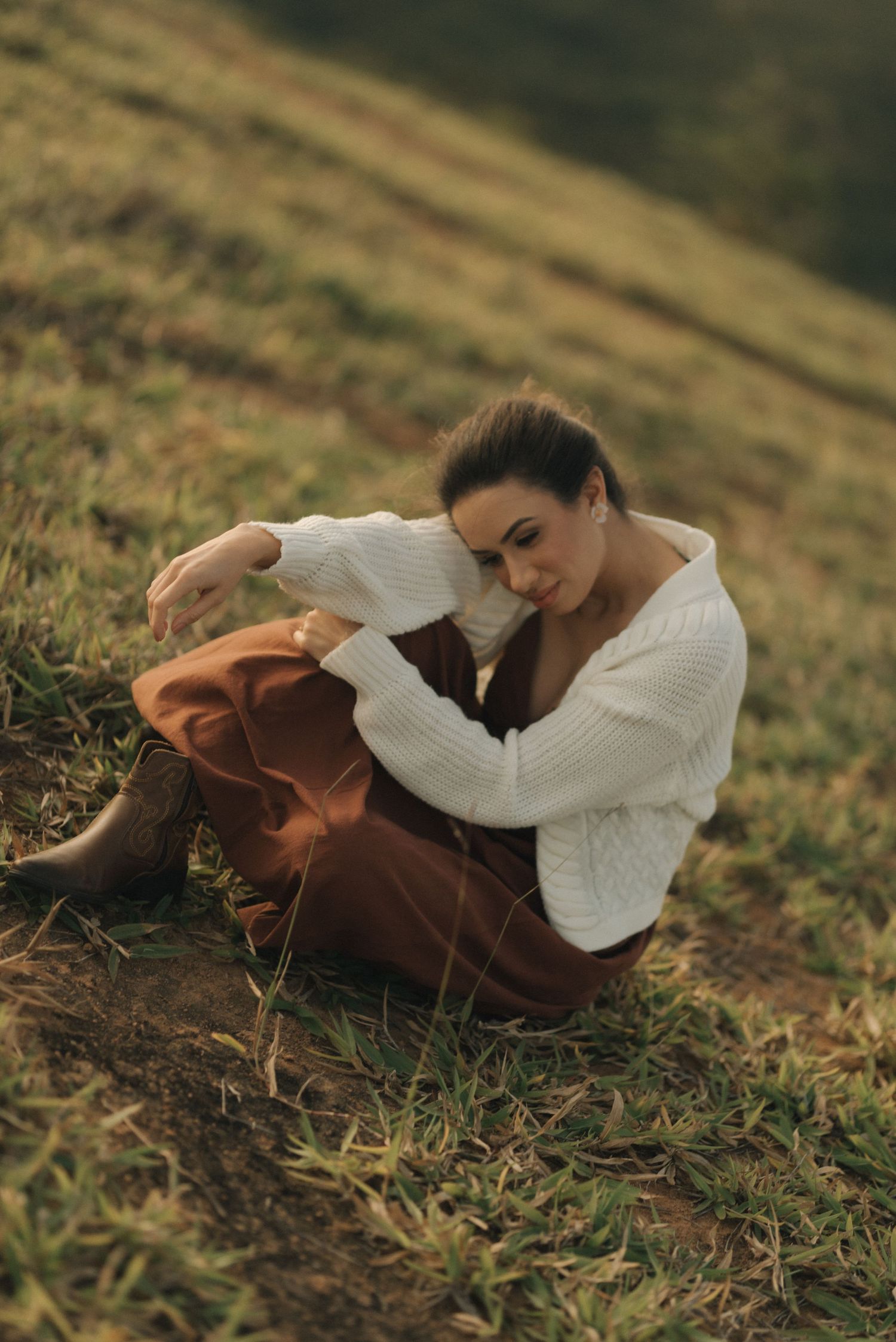 Cozy autumn portrait featuring a white sweater and rust-colored pants on a grassy slope.