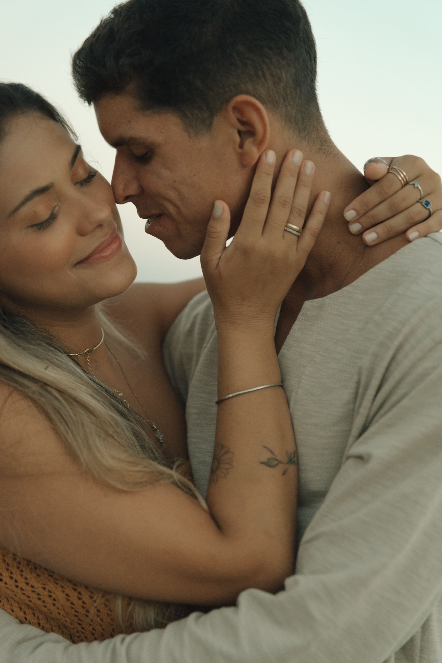 Intimate closeup of couple embracing, showing rings and jewelry in warm natural lighting.