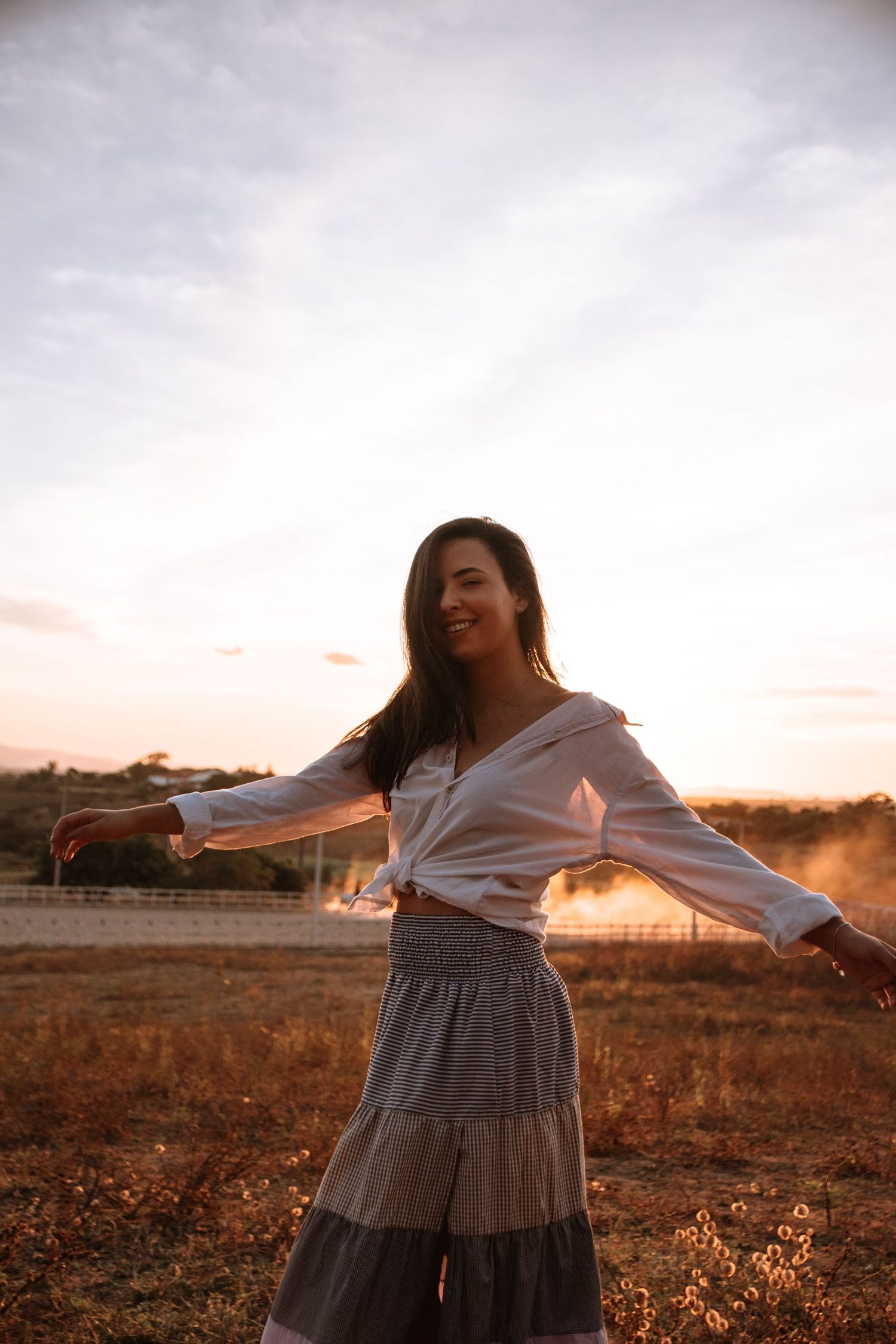 Dancing figure spins freely in a golden field during sunset wearing a flowing tiered skirt.