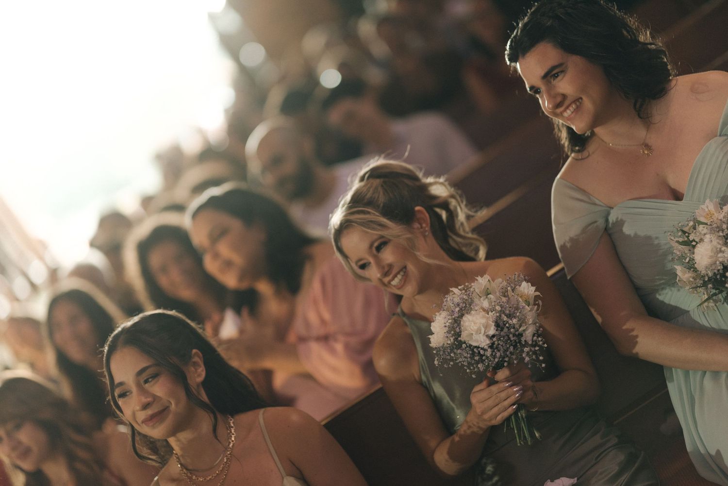 Wedding party members share joyful laughter while holding bouquets during a celebration.