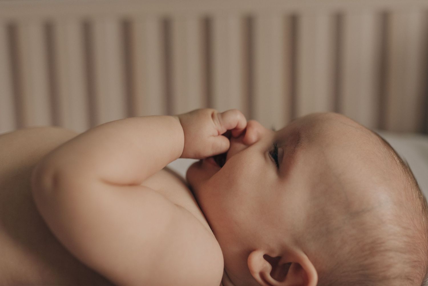 Close-up profile view of baby lying on soft bedding in natural light.