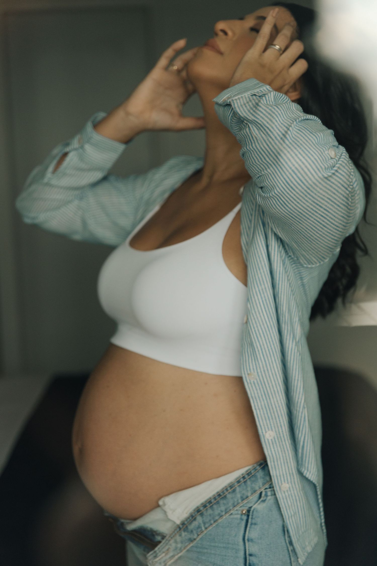 Casual maternity portrait showing pregnant belly with striped button-up shirt and white crop top.