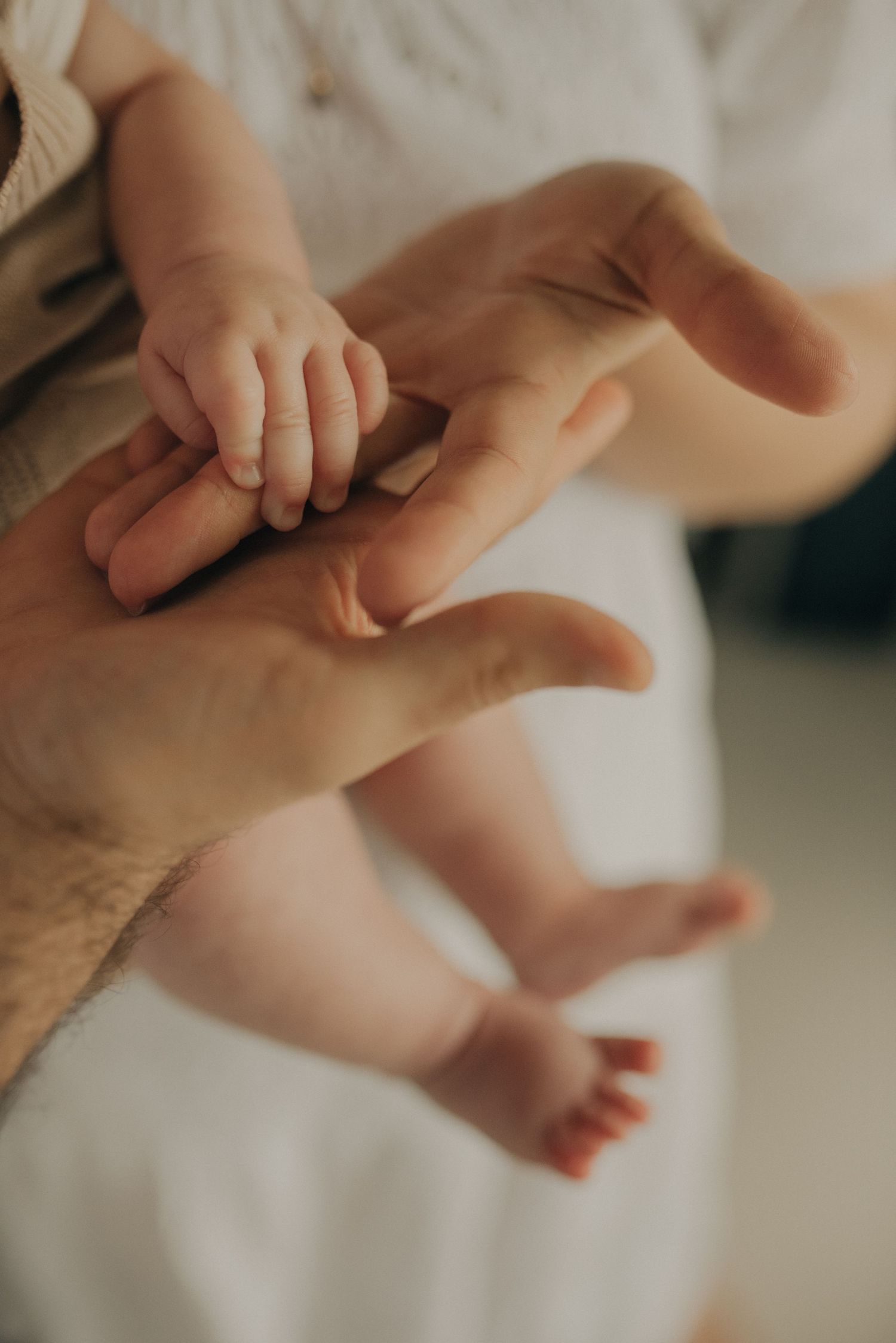 Close-up of a baby's tiny hand grasping an adult's finger in soft natural light.