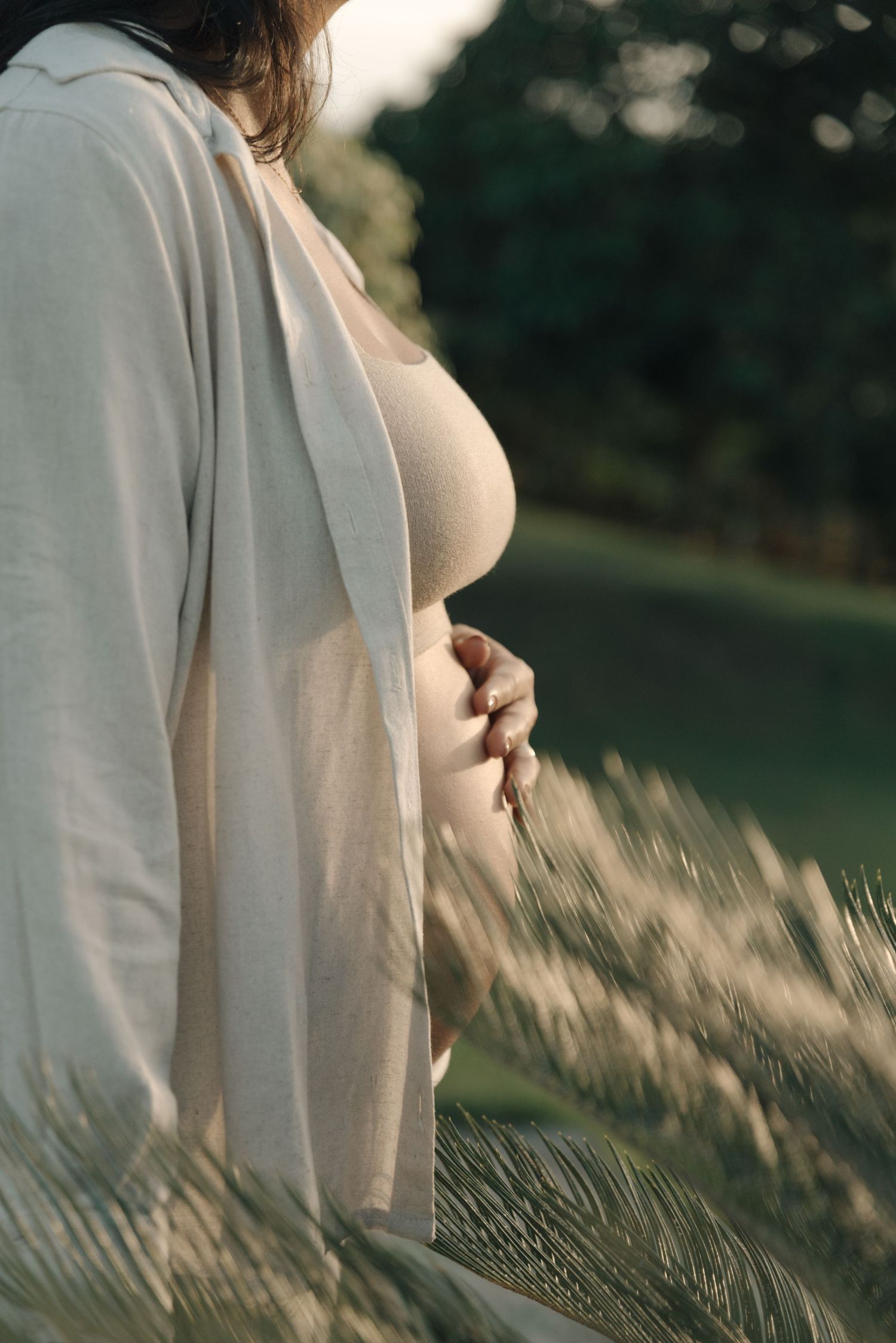 Side view maternity portrait in natural setting with white flowing fabric and golden light.