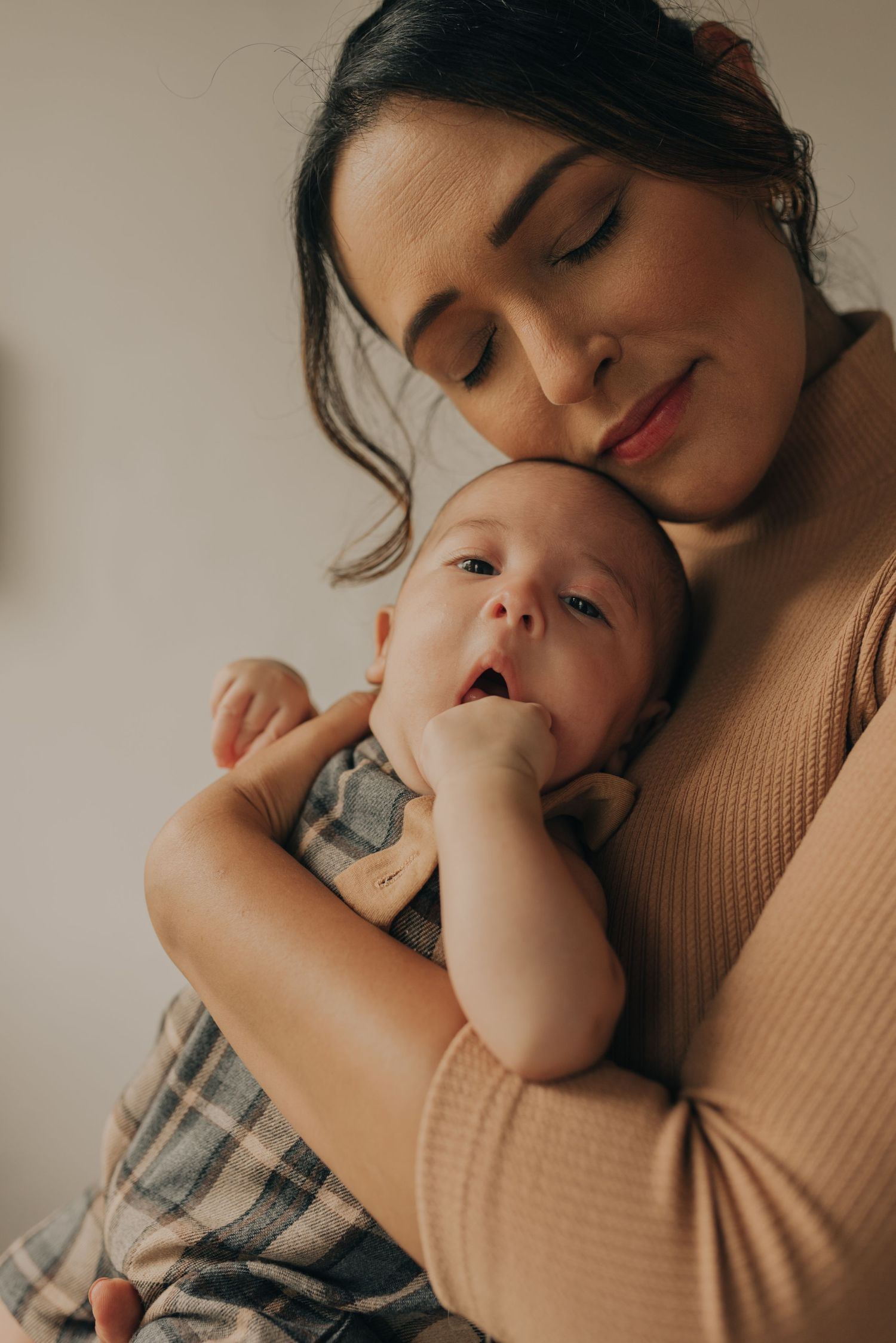 A tender moment between parent and infant as they embrace in warm lighting wearing neutral tones.