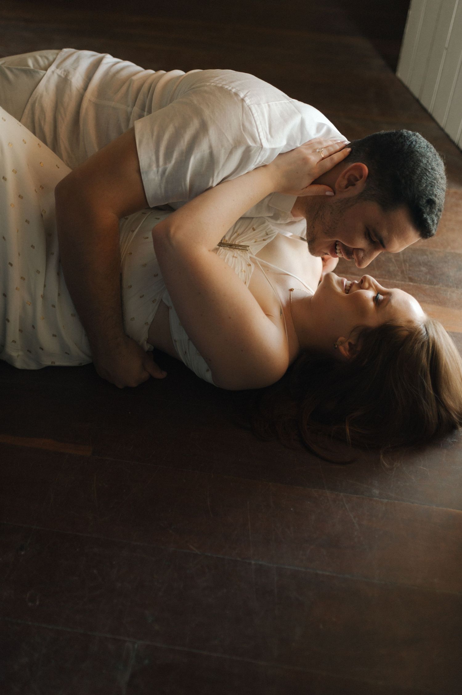 Two people share an intimate moment lying on a wooden floor.