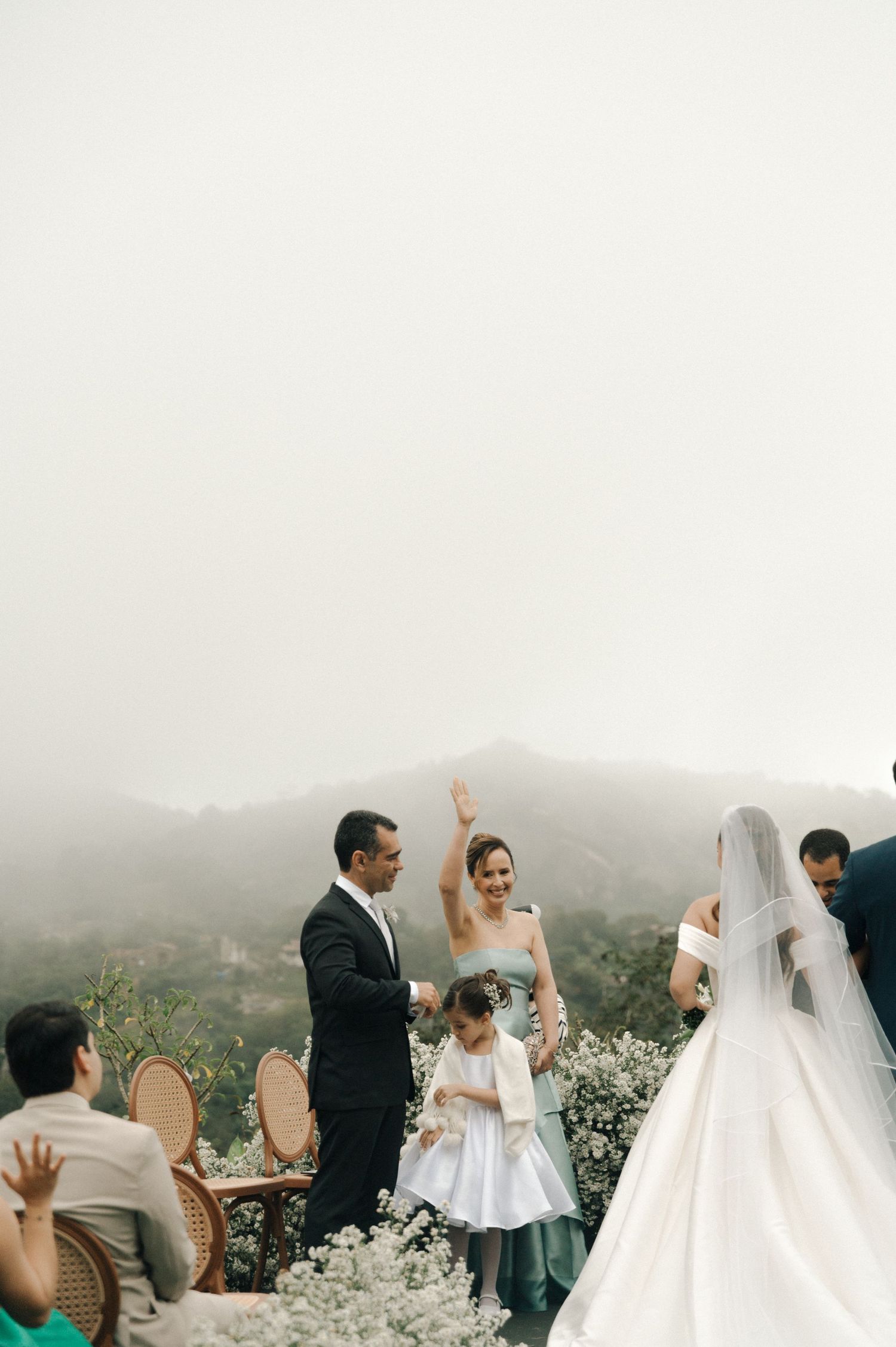 A misty outdoor wedding celebration with guests gathered on a mountain terrace surrounded by lush greenery.
