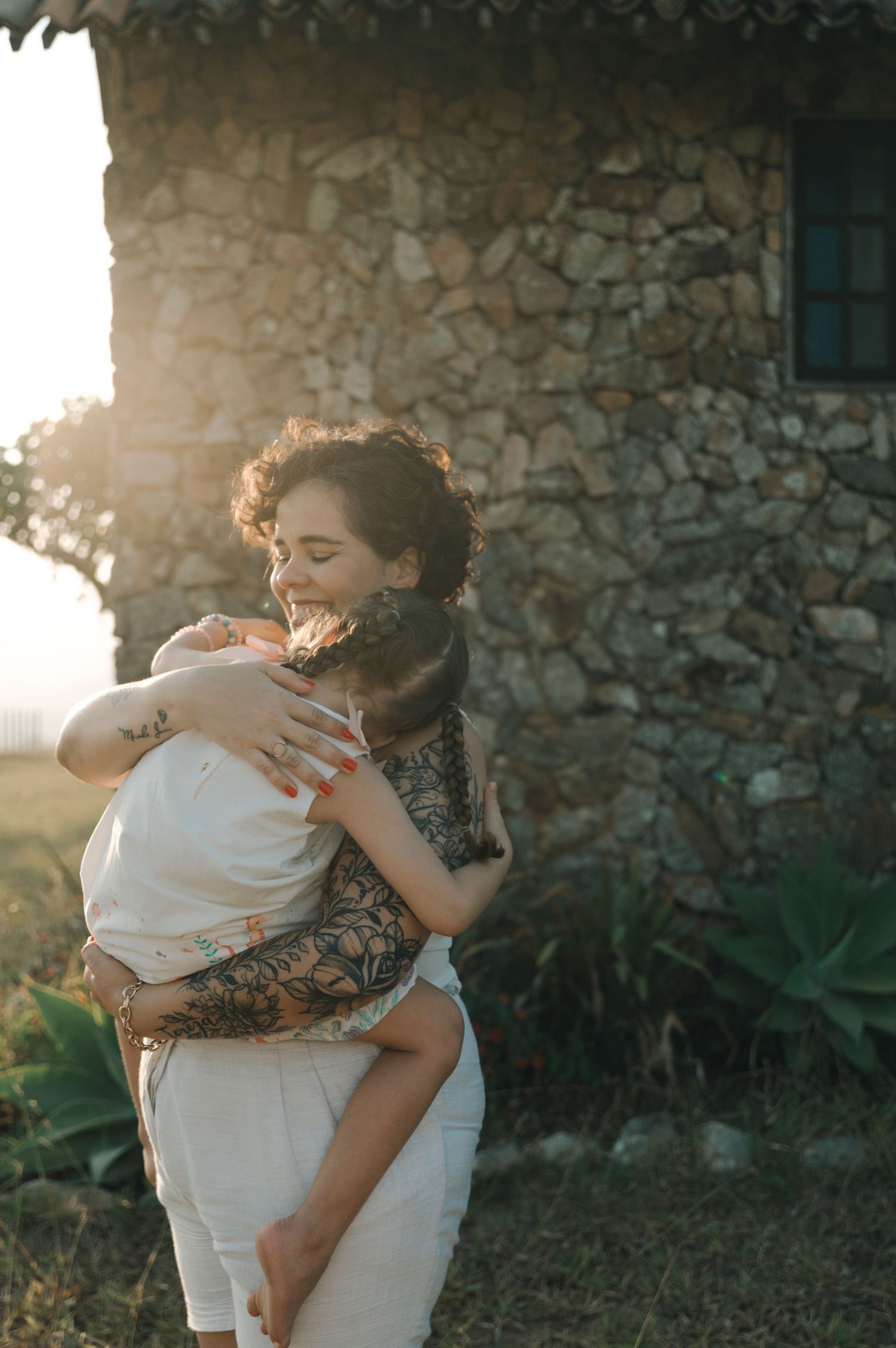 Two people share an intimate embrace against a rustic stone wall backdrop during golden hour sunset.