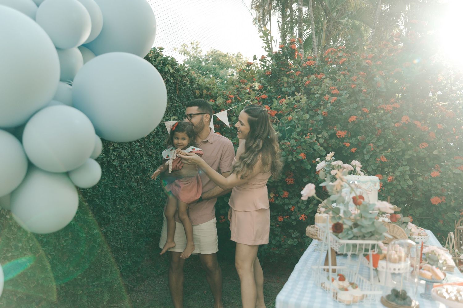 Elegant outdoor baby shower celebration with white and blue balloon decorations and guests gathering in a sunny garden setting.