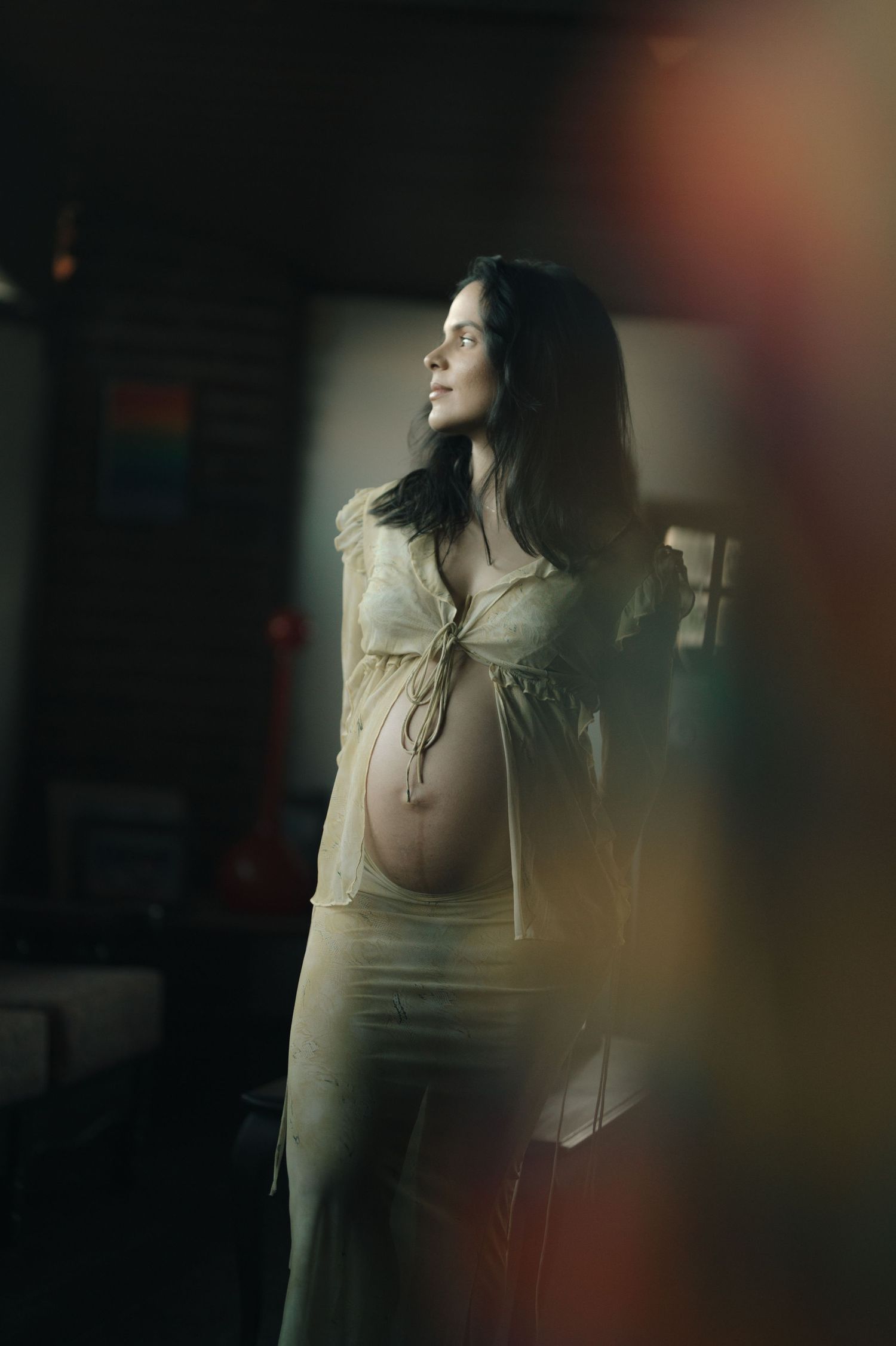 Artistic maternity portrait with soft lighting shows an expectant mother in a cream-colored top gazing to the side.
