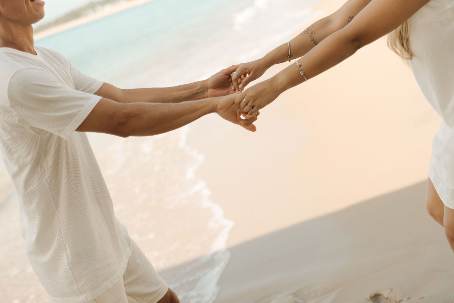 Close up of couple holding hands tenderly against beach background.