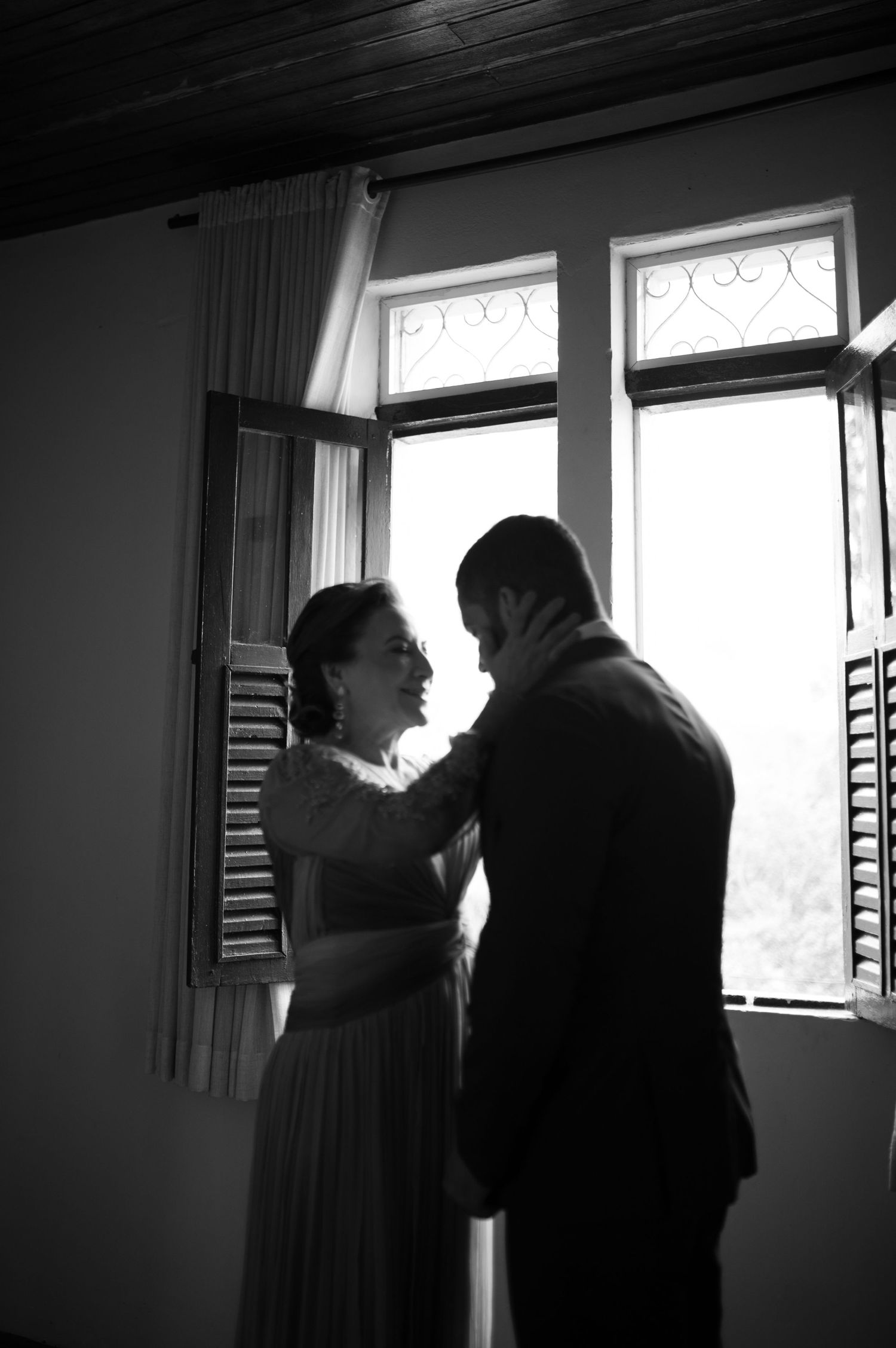 A romantic silhouette of newlyweds sharing an intimate moment by a window in black and white.