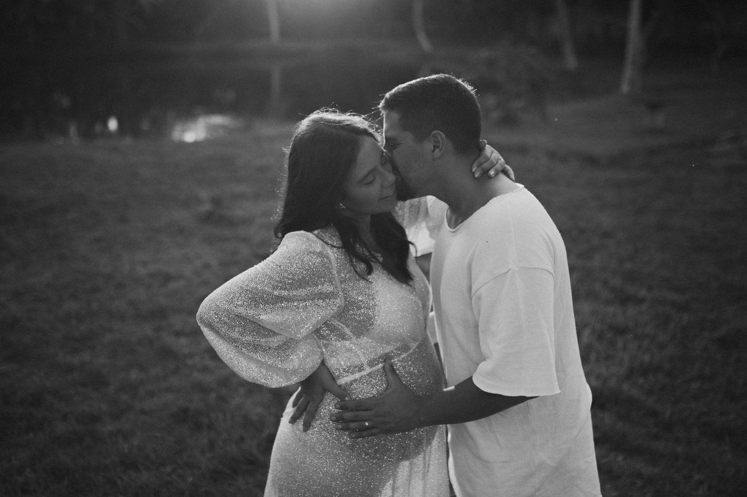 A romantic black and white portrait of a couple in casual attire embracing outdoors.