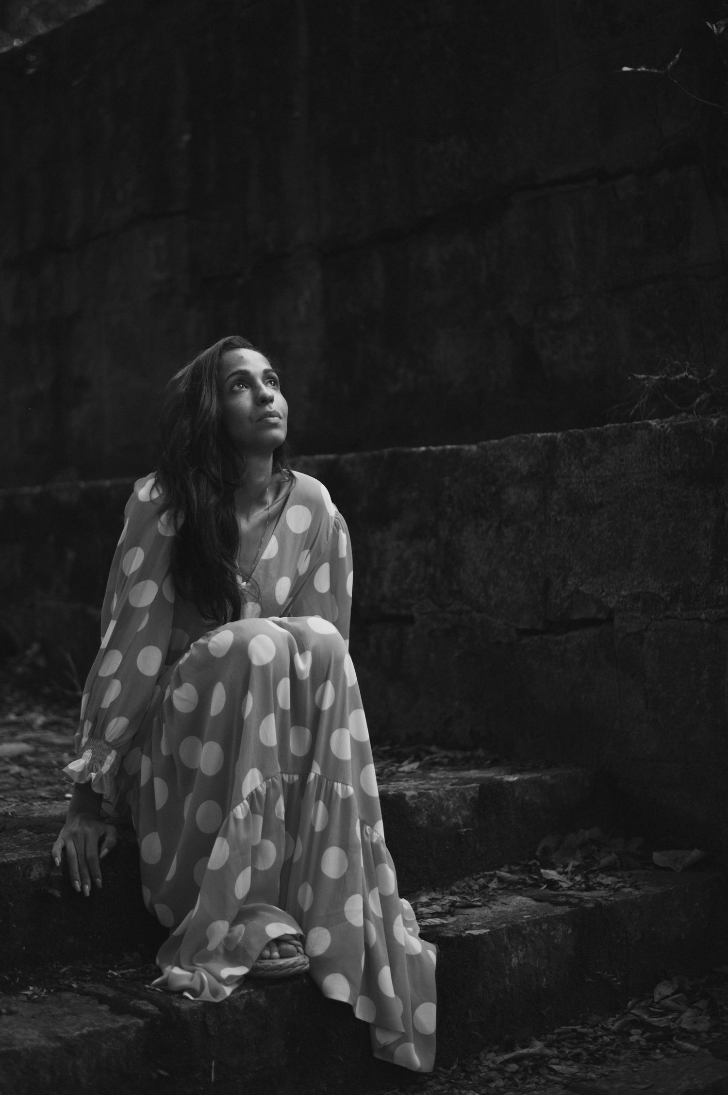 Dramatic black and white photo of person in polka dot dress sitting on stone steps.