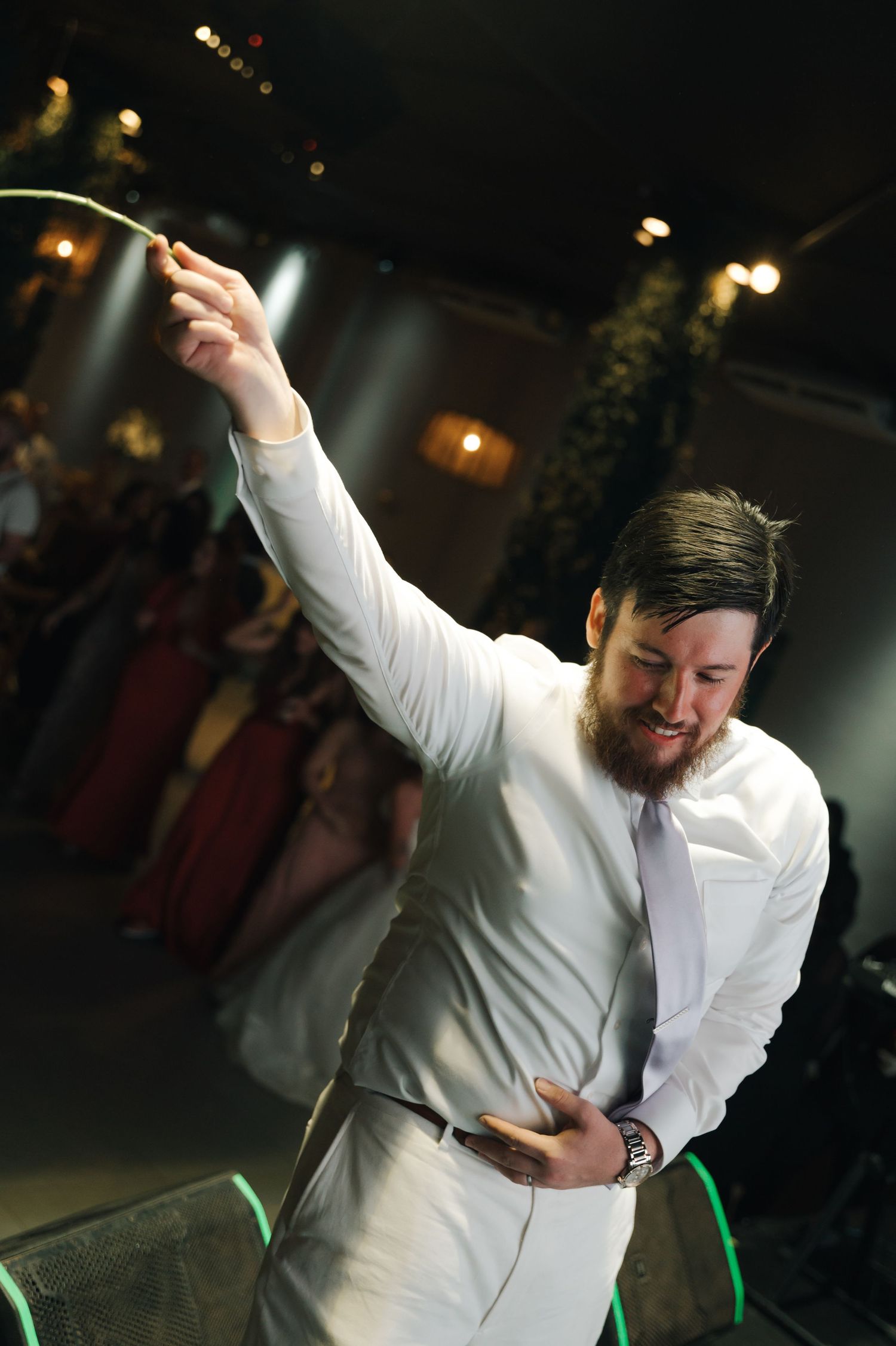 Person in white shirt dancing with raised arm in dark room with bokeh lights in background.