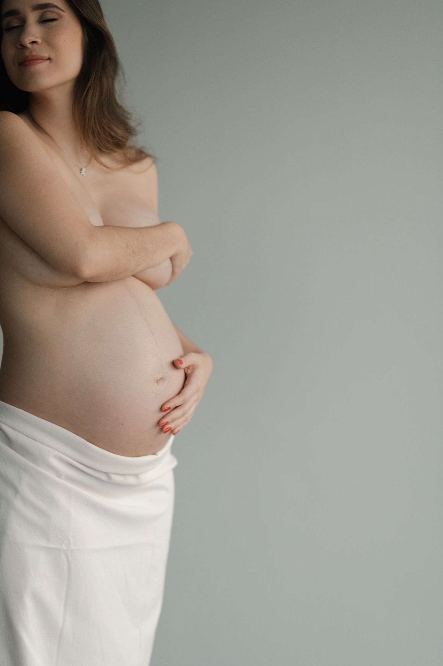 Intimate maternity portrait showing bare pregnant belly against light grey background.
