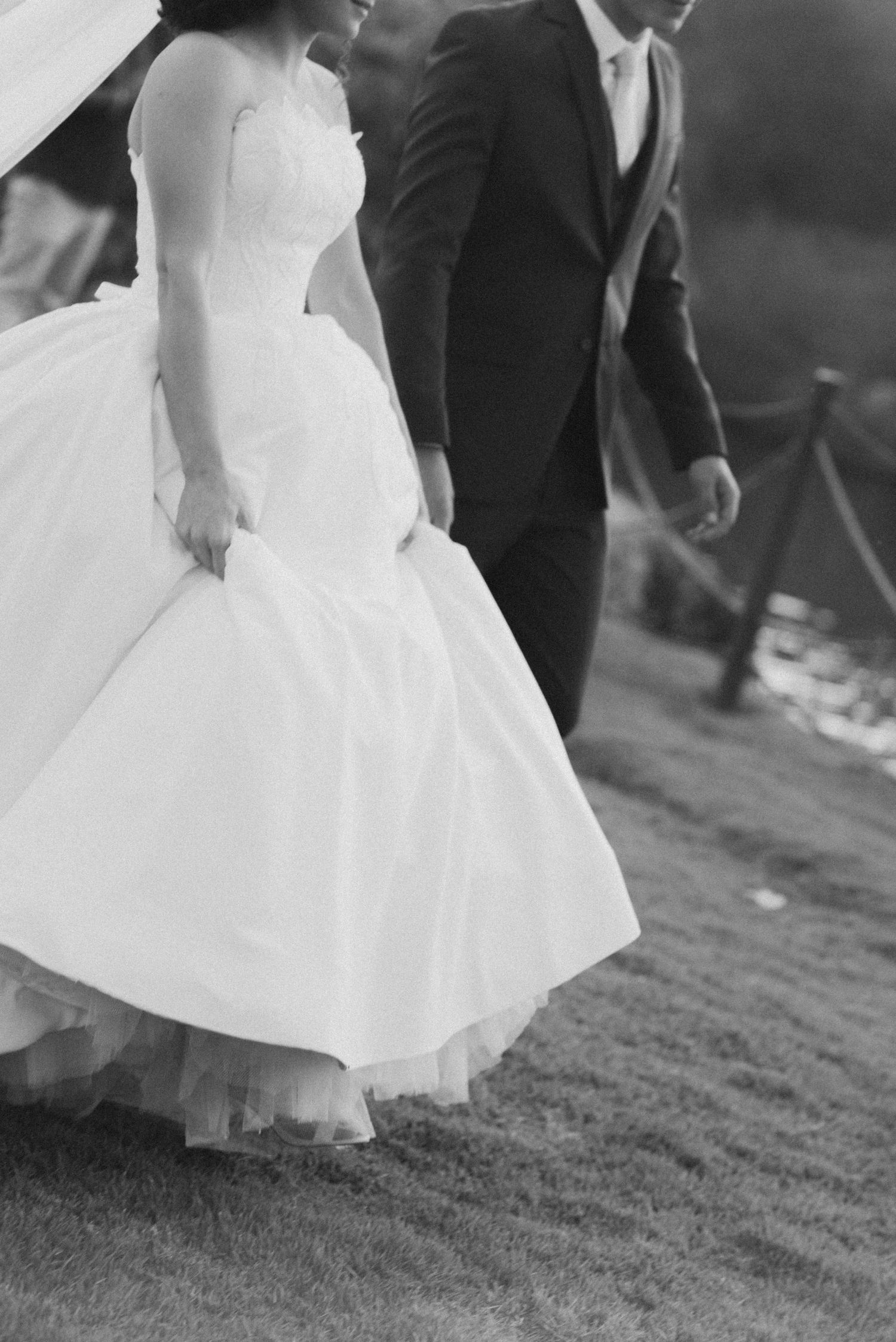 A close-up of a bride's ballgown skirt and groom's suit while walking.