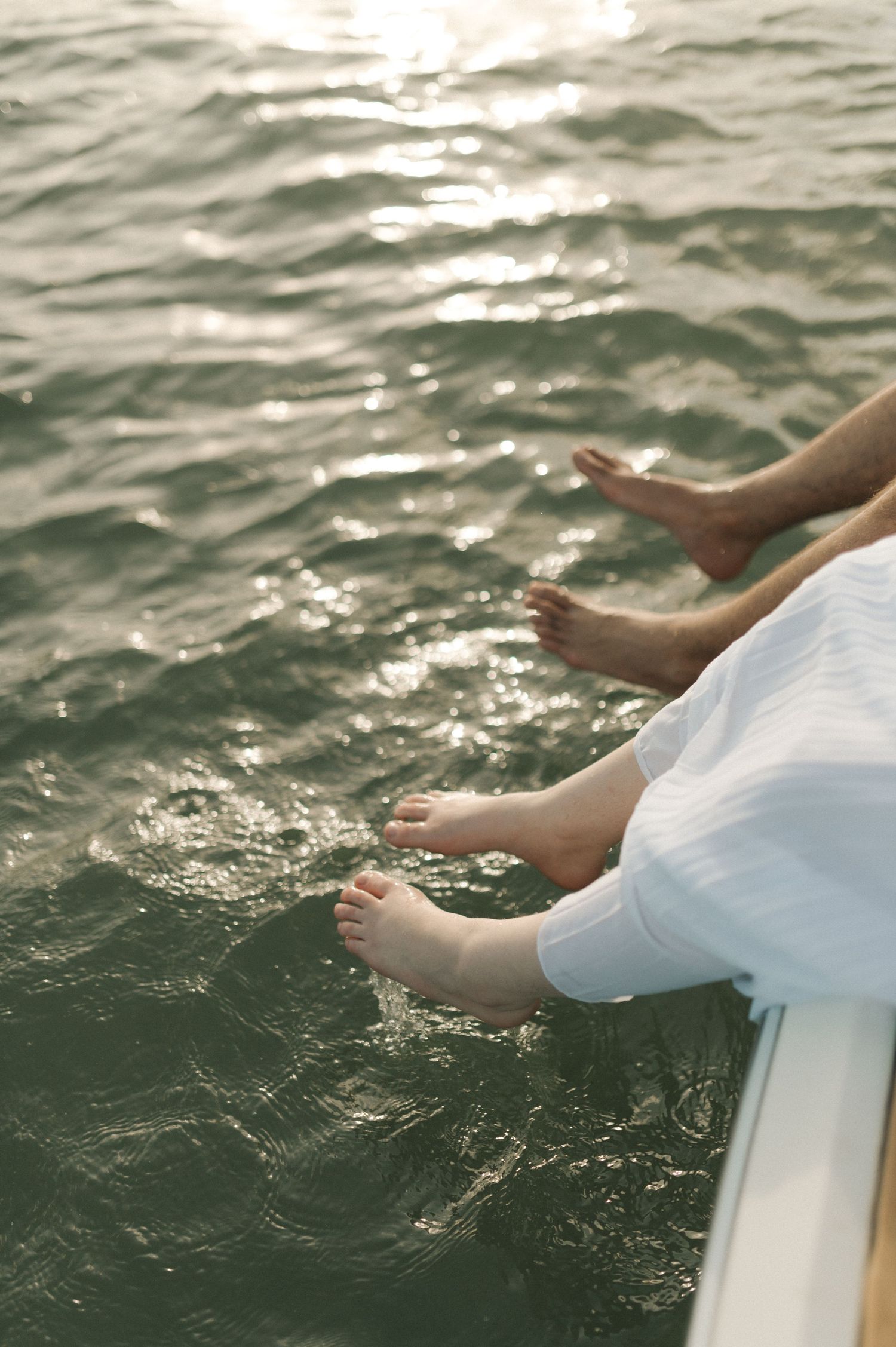 Bare feet dangling over sparkling water from a boat on a sunny day.