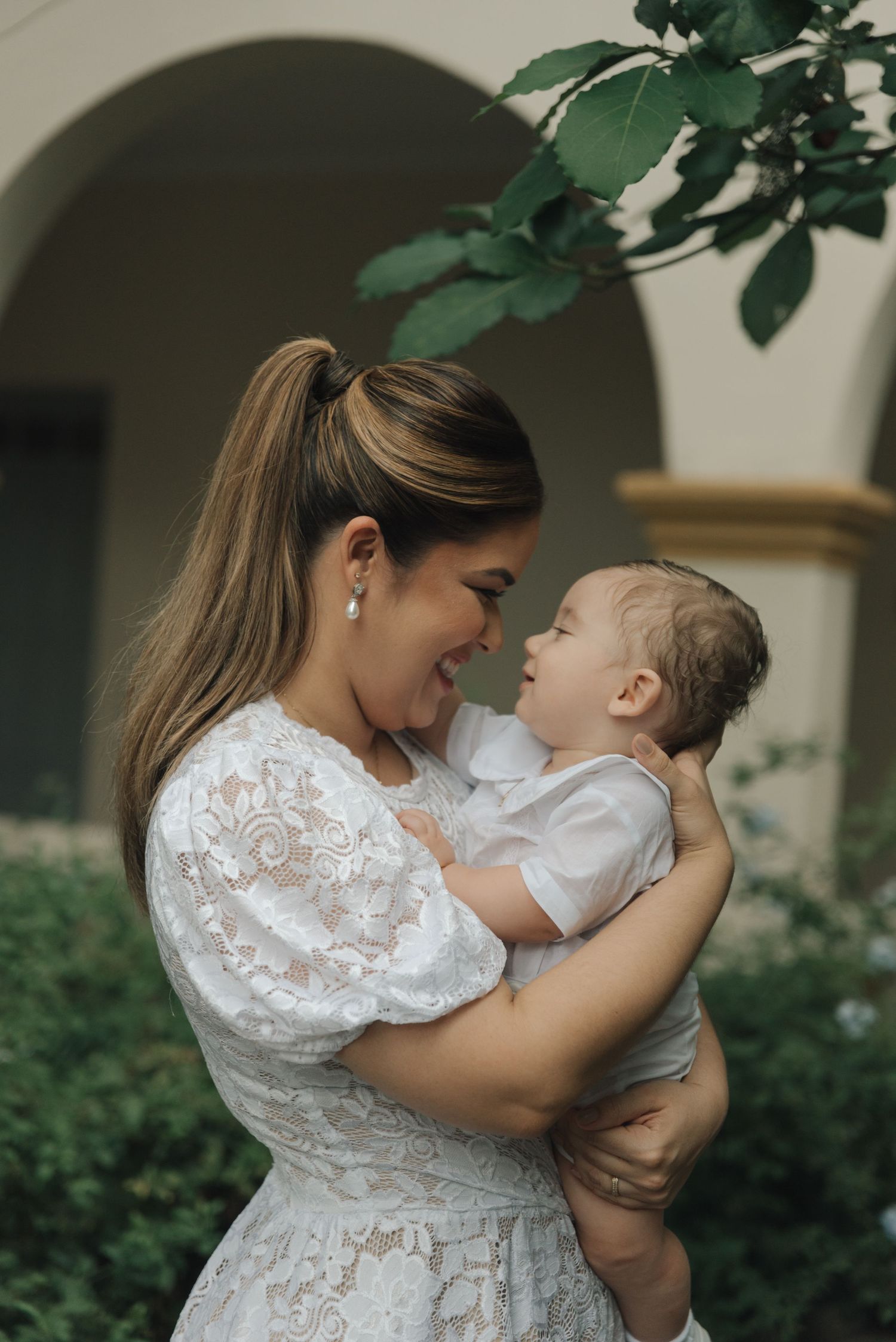 A tender moment captured between two people in a garden setting with lush greenery in the background.