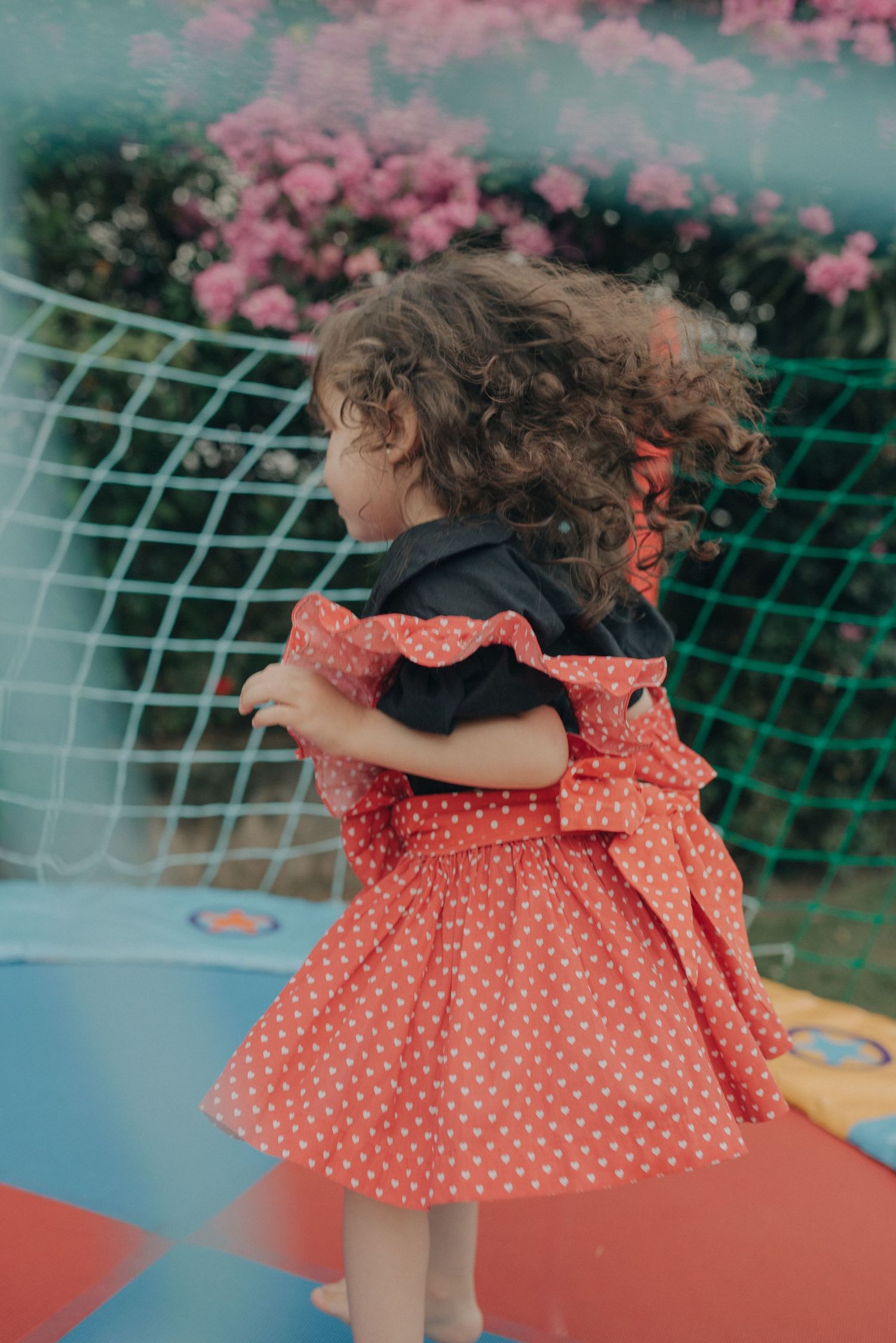 Young child in polka dot dress playing outdoors with pink flowers in background.