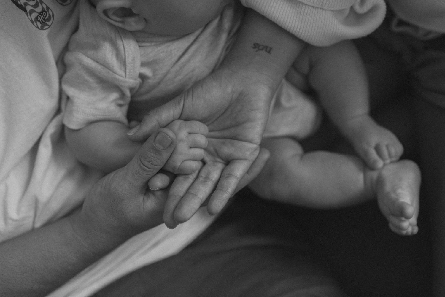 Close-up black and white shot of adult's hand holding baby's tiny hand.