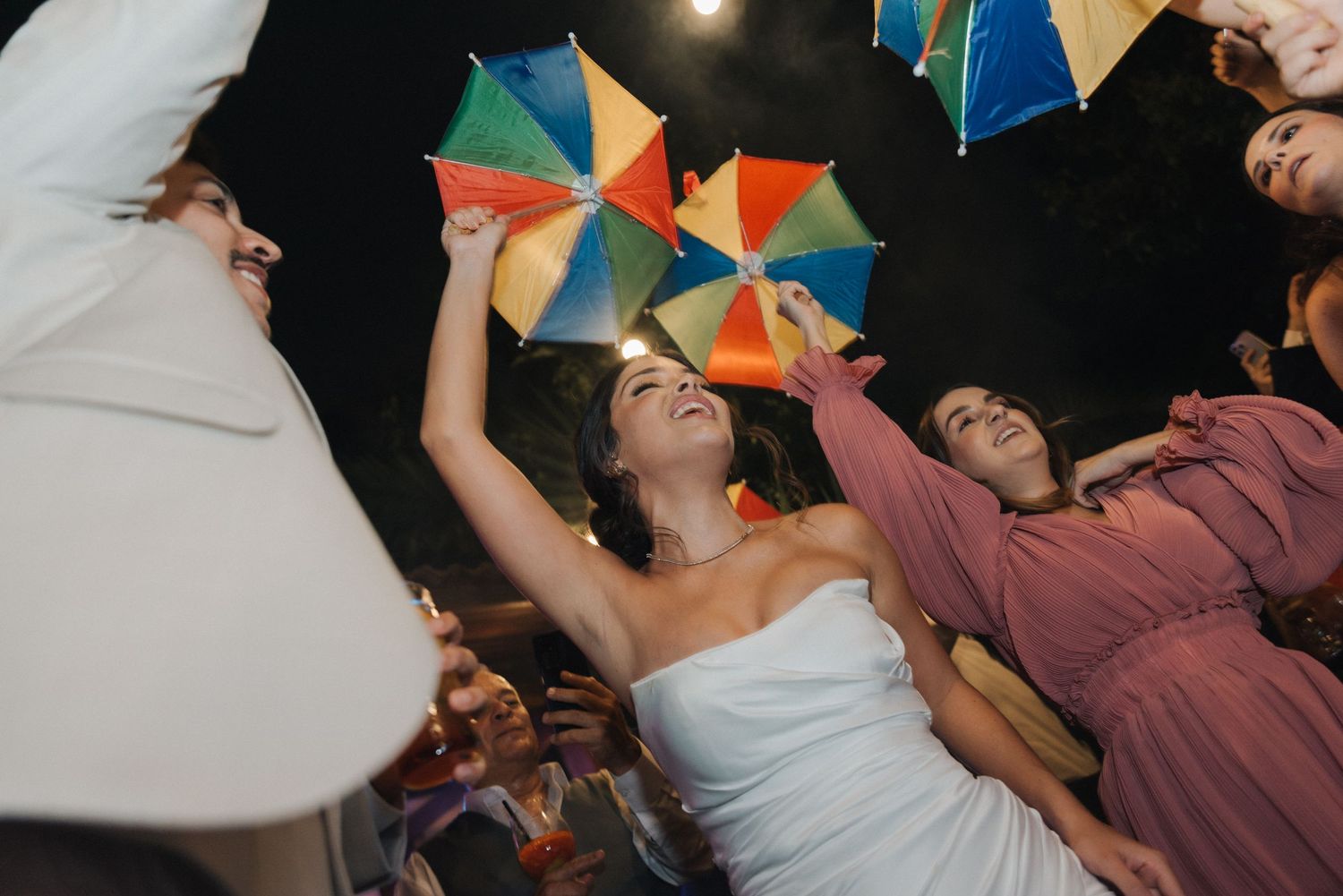 Wedding guests hold colorful umbrellas during a nighttime celebration.