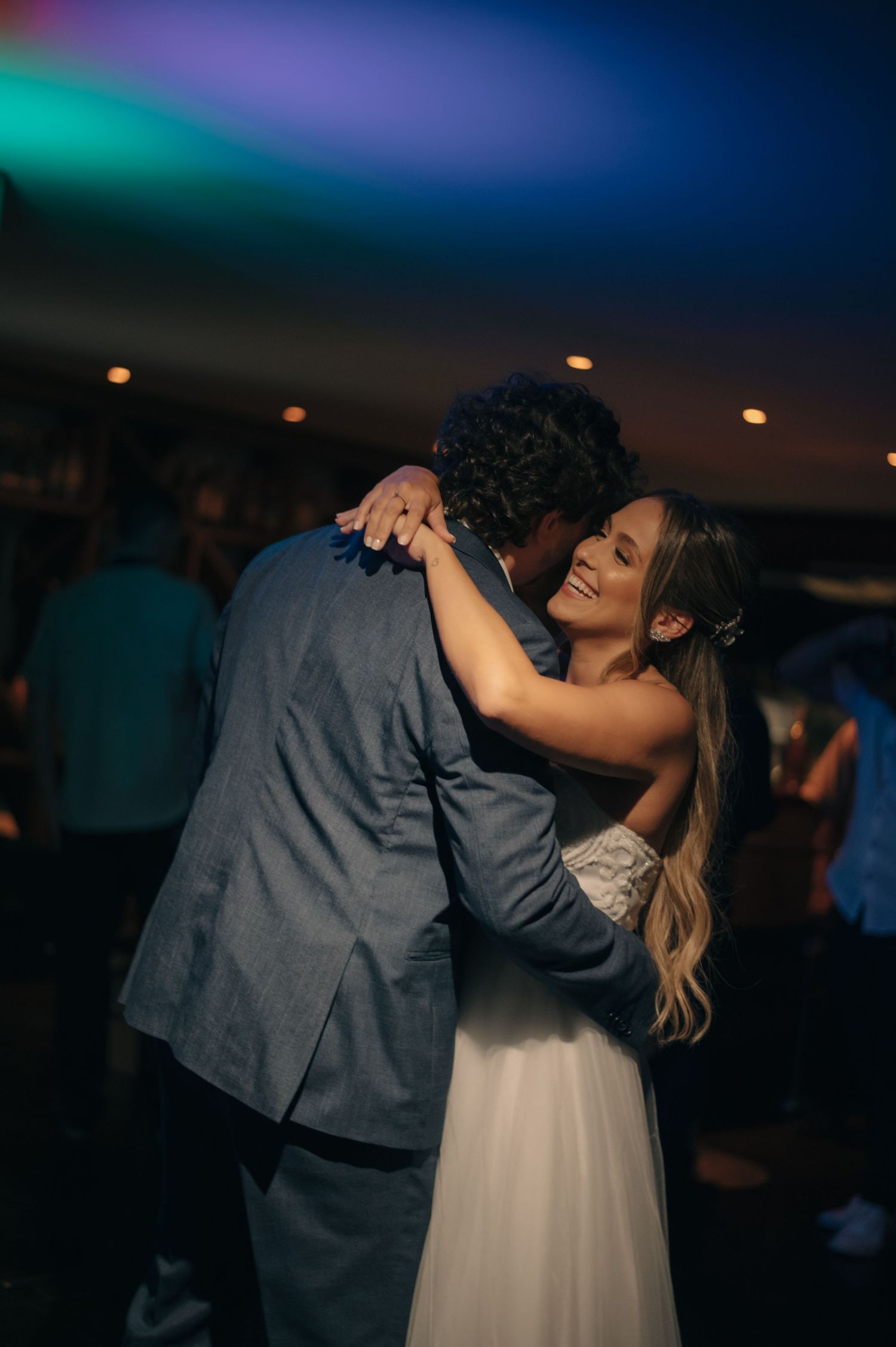 A couple shares an intimate dance moment under colorful reception lighting.